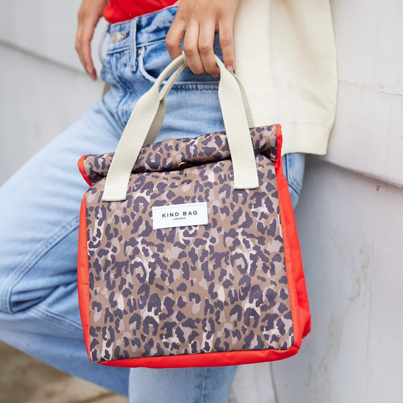 Person holding a leopard print bag with red accents, wearing a red shirt and light blue jeans.