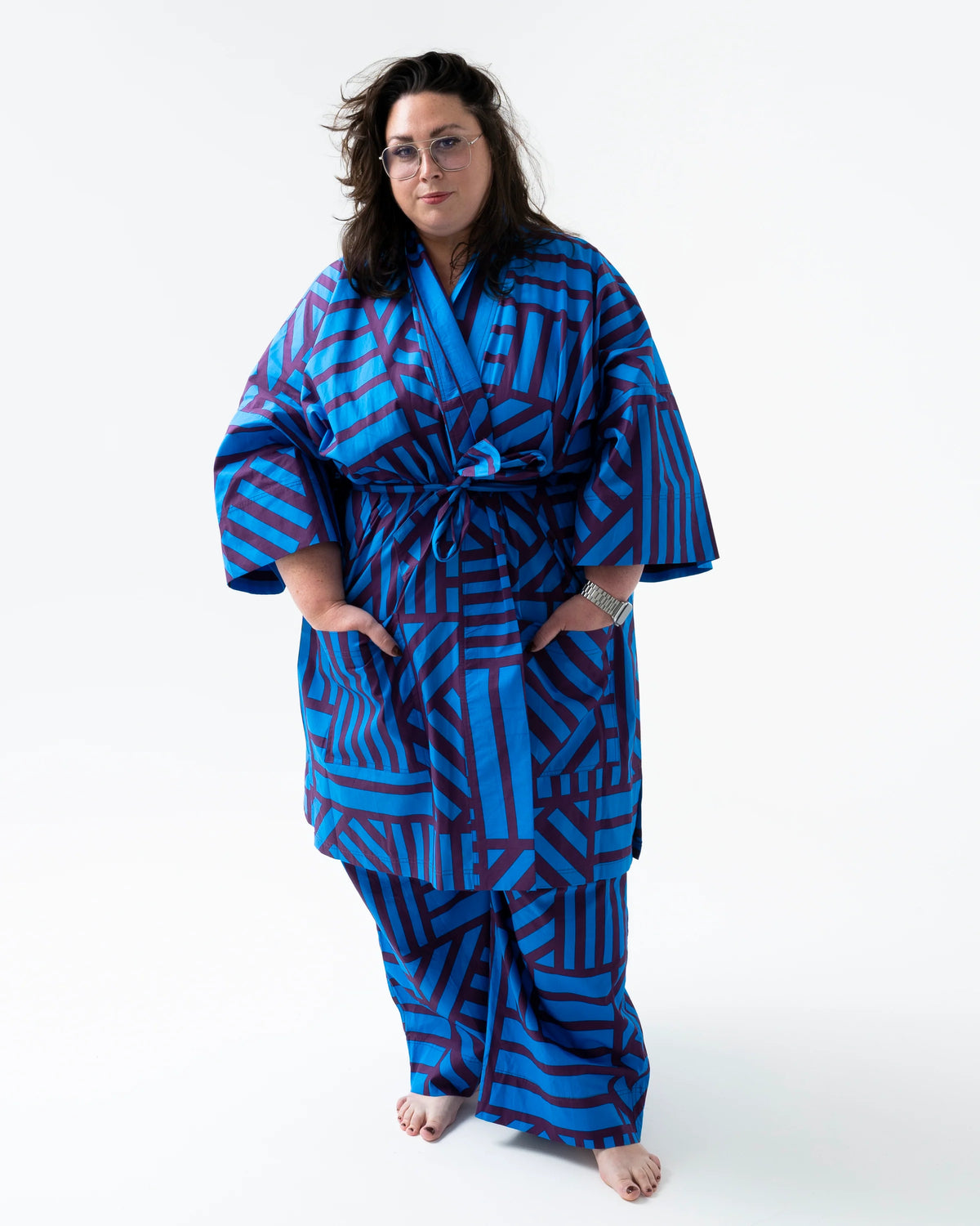 A woman modeling a blue and red geometric patterned kimono robe and matching pants against a plain white studio background.