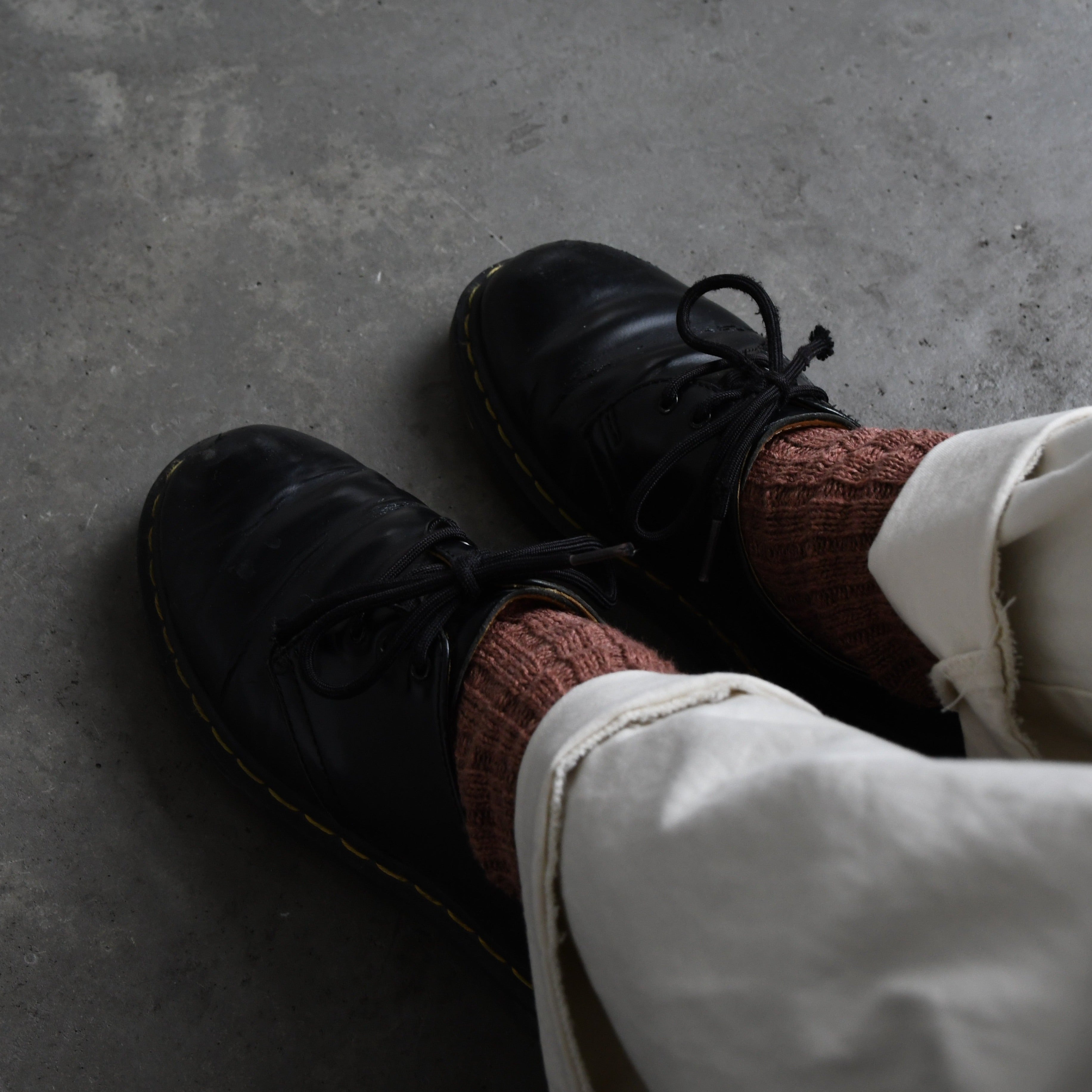 Pair of black leather lace-up shoes with yellow stitching, worn with mauve socks.