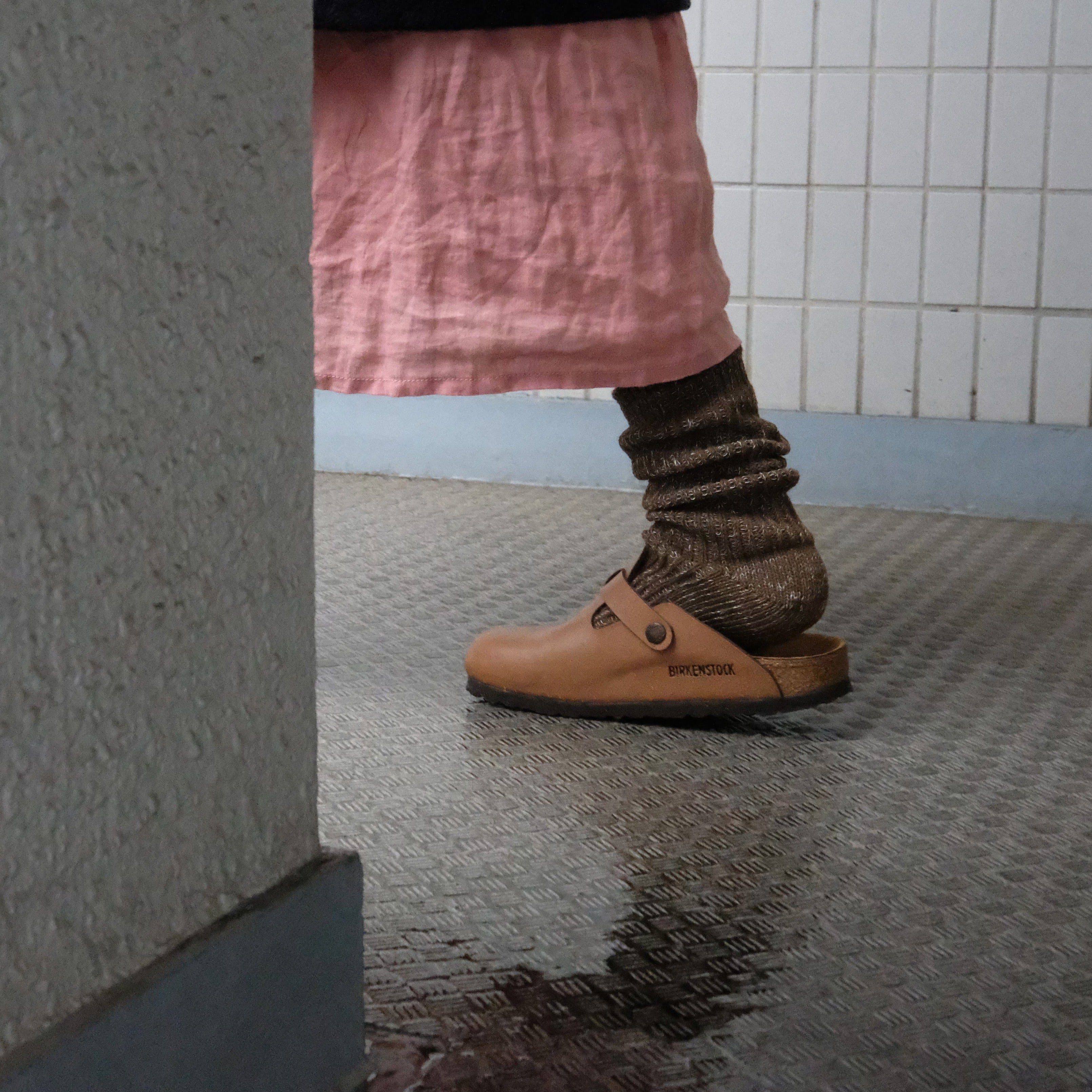 Tan leather Birkenstock clog with a single strap and buckle, worn with brown wool socks.