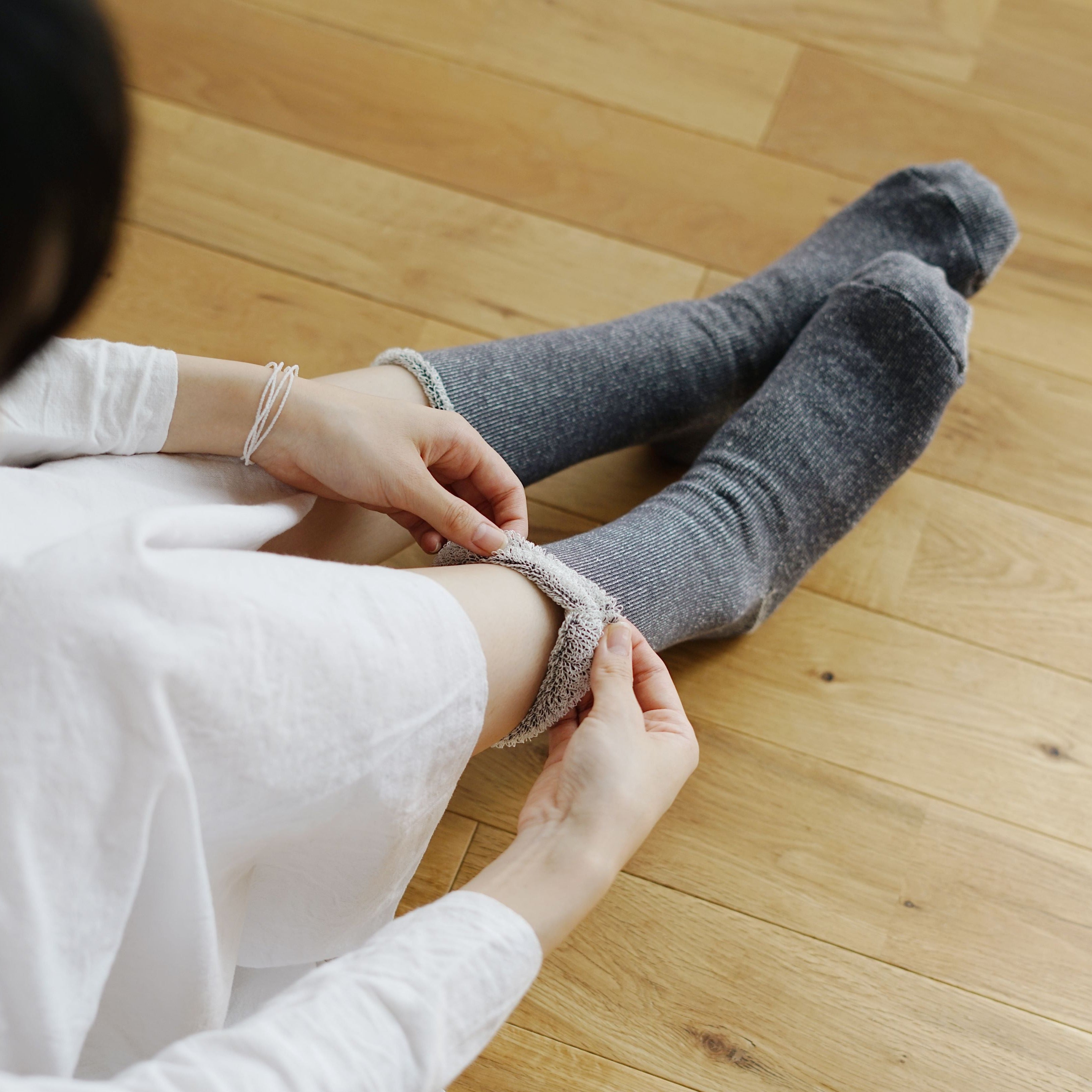 A person puts on a pair of long, gray ribbed socks with a fluffy, off-white cuff.