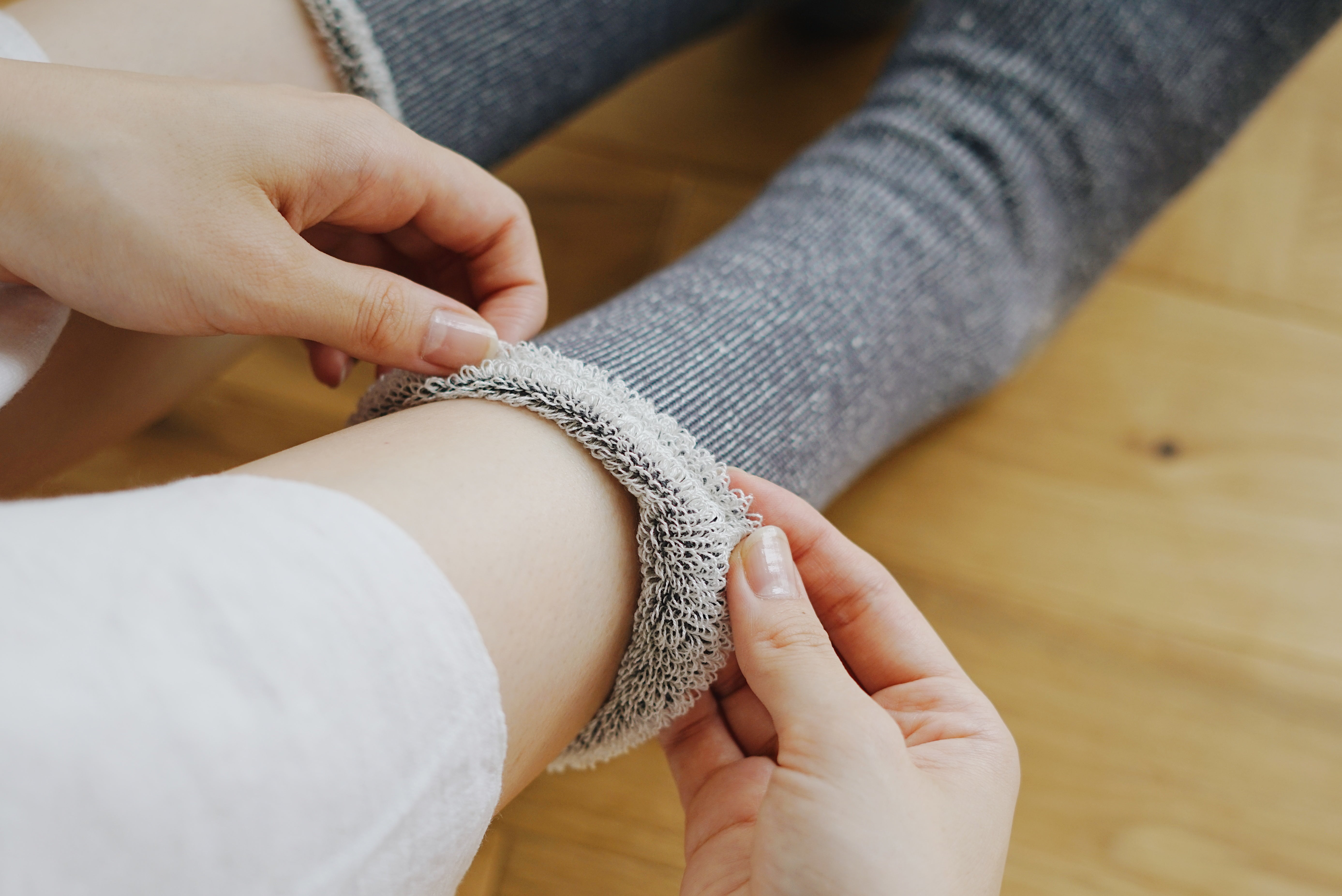 A pair of gray ribbed socks with a textured cuff is being put on.  The socks appear soft and comfortable.