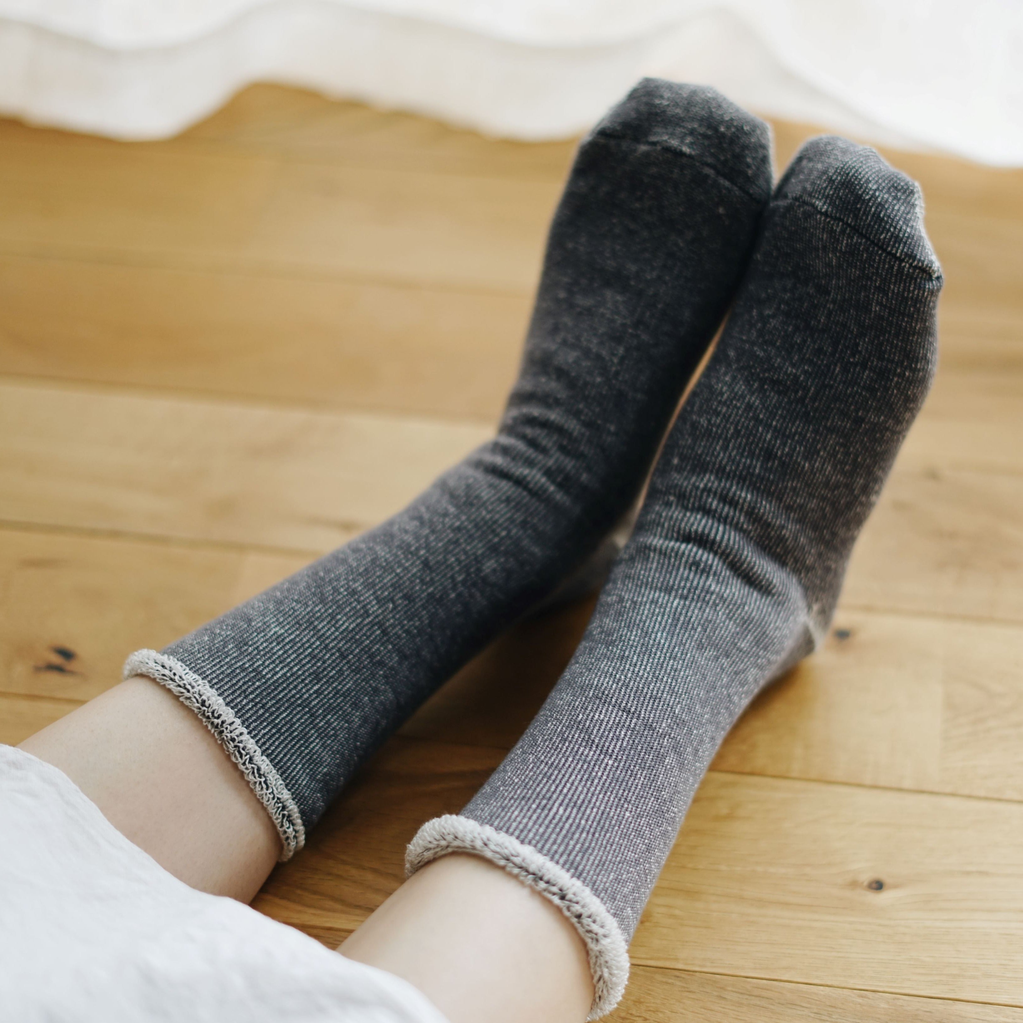 Pair of dark gray ribbed socks with a light gray fluffy cuff, lying on a wooden floor.