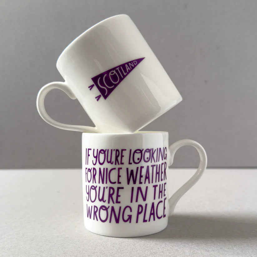 Two white mugs stacked; one features a purple Scotland pennant, the other says "If you're looking for nice weather you're in