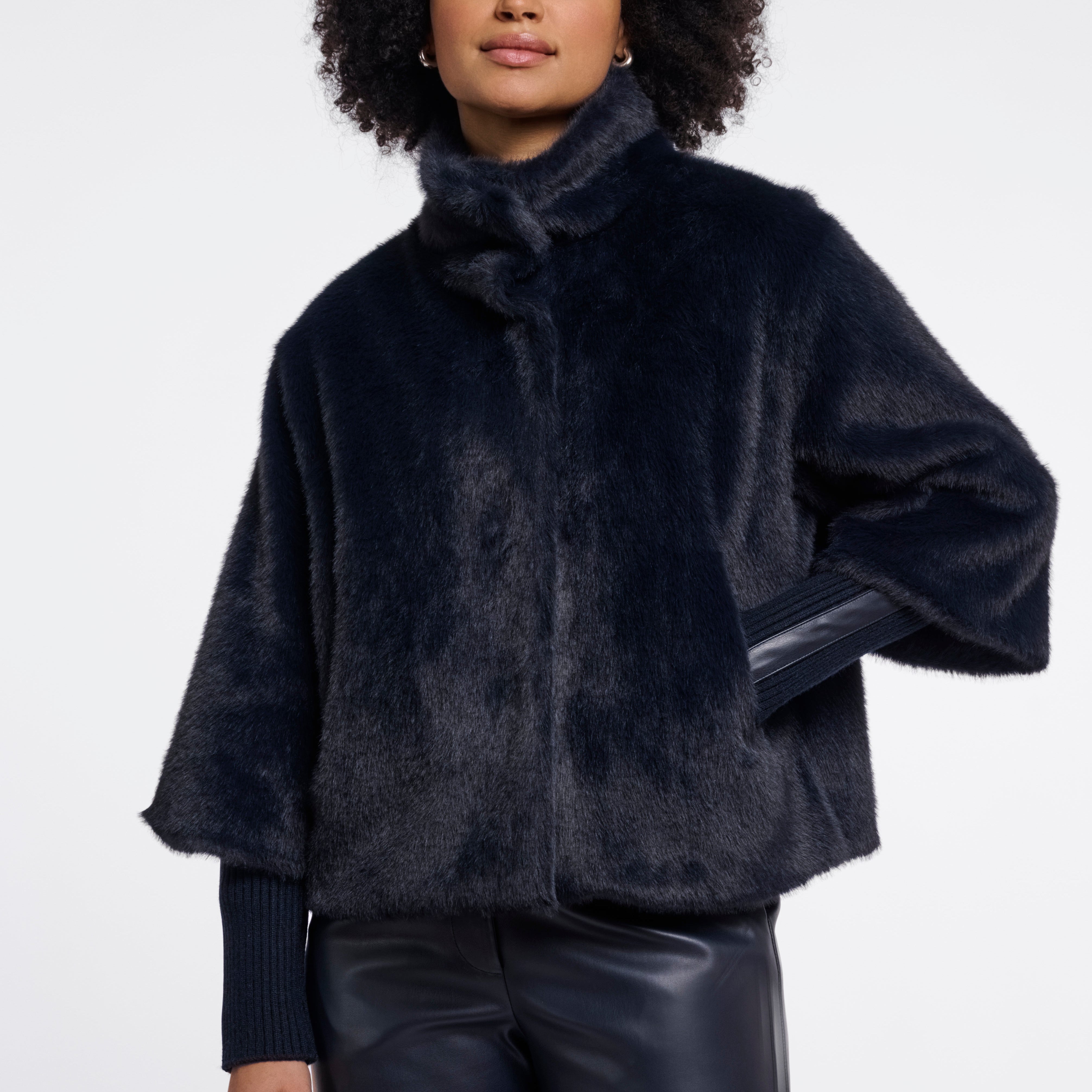 Woman wearing a dark blue faux fur jacket on a white background