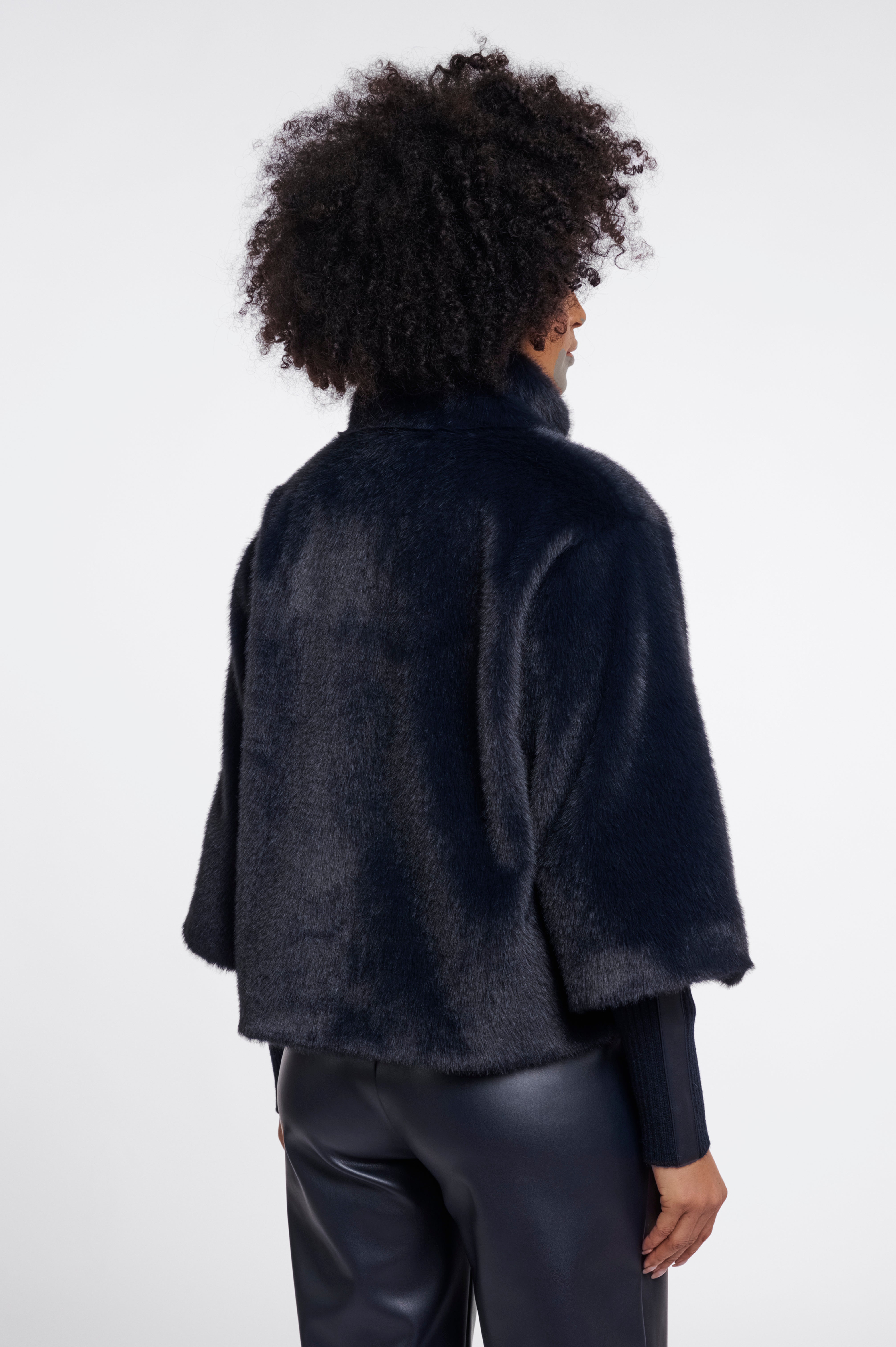 Person wearing a dark blue textured jacket and black pants on a white background