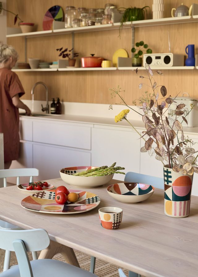 Colorful tableware on a kitchen table with a person in the background.