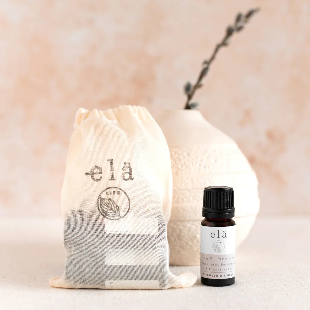 elä diffuser oil blend in a dark amber glass bottle, next to a muslin bag containing dark brown diffuser reeds, both with