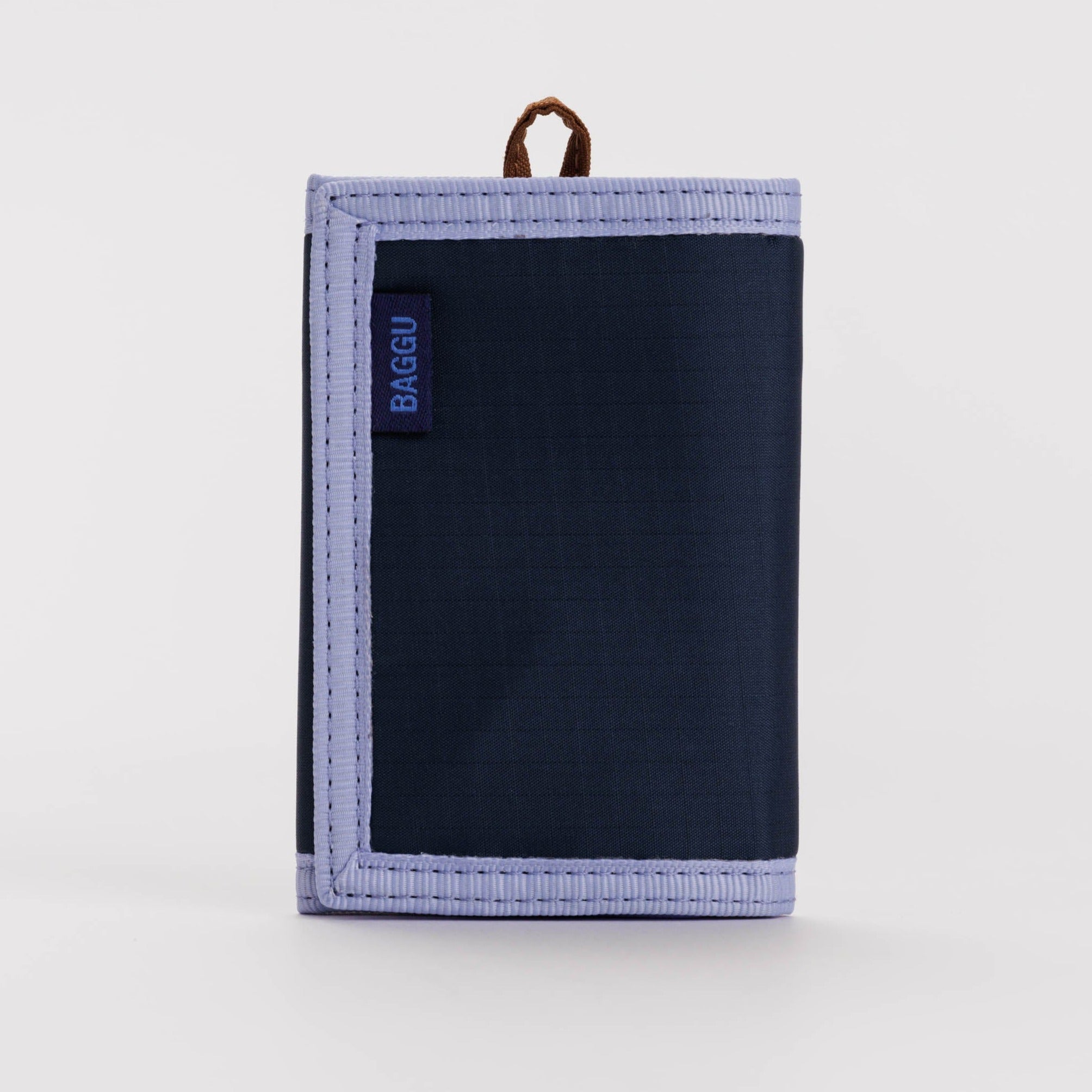 Navy blue Baggu tri-fold wallet with light purple trim and a brown leather pull tab.