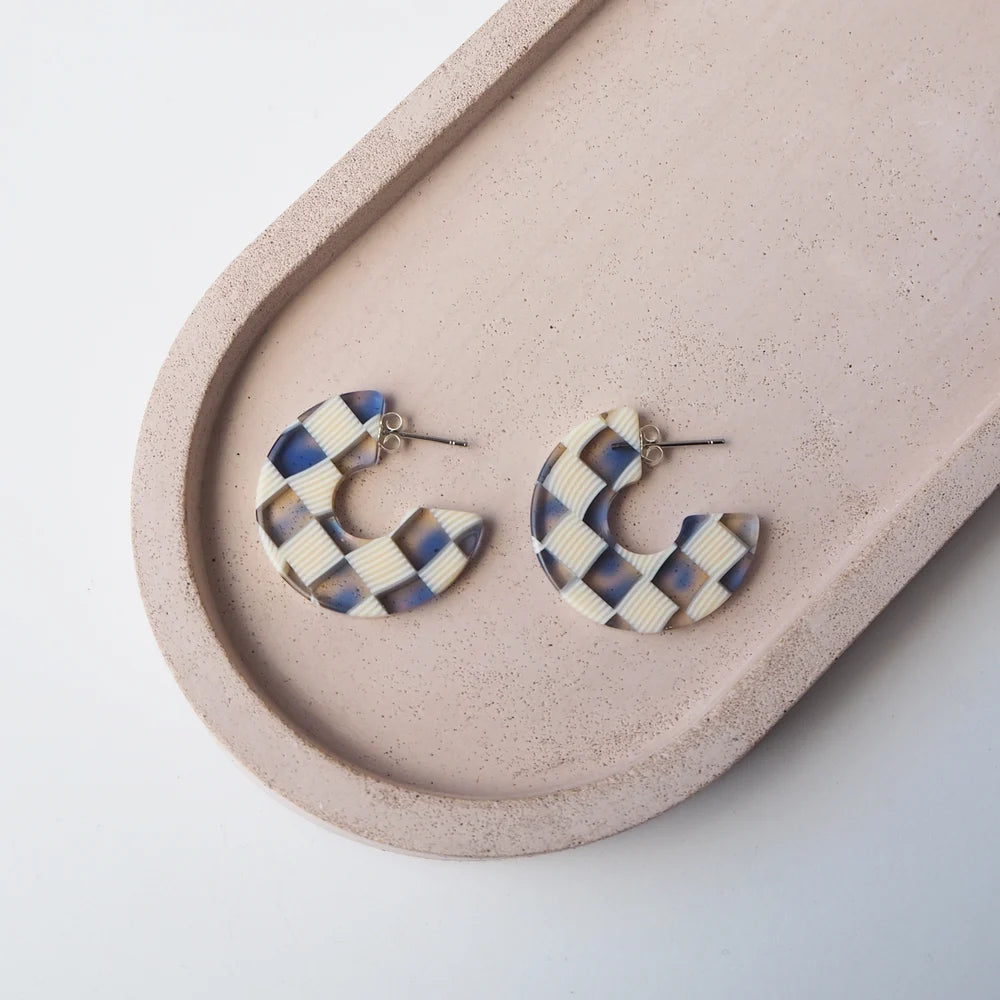 Pair of cream and blue checkered semi-circle hoop earrings.