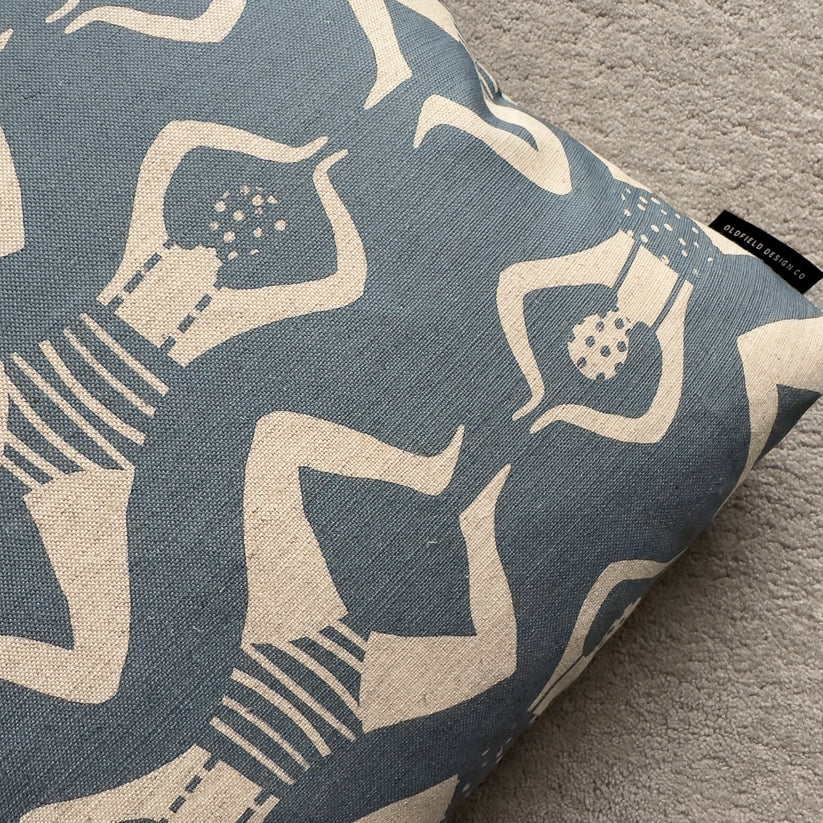 Blue cushion with a repeating pattern of off-white stylized figures.