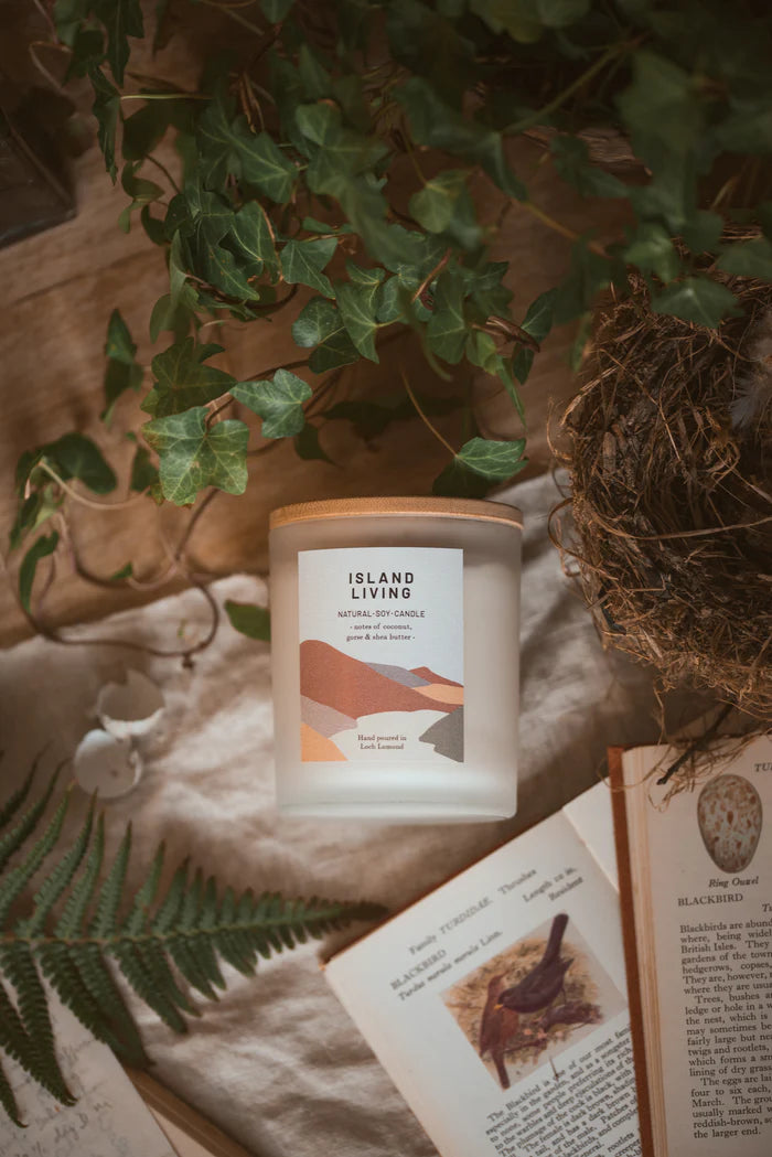 Island Living natural soy candle in frosted glass jar with bamboo lid; minimalist label with landscape graphic.