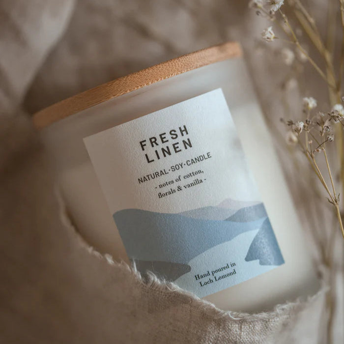 Frosted glass Fresh Linen soy candle with wooden lid; label features light blue abstract design and notes of cotton,