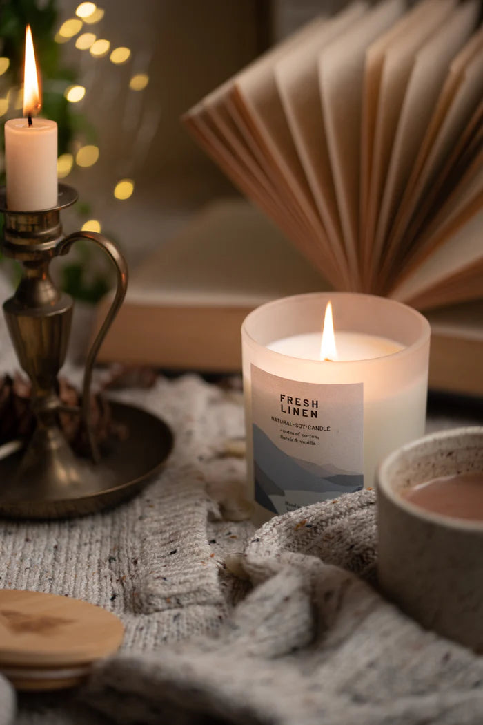 Lit "Fresh Linen" natural soy candle in frosted glass jar with minimalist label.