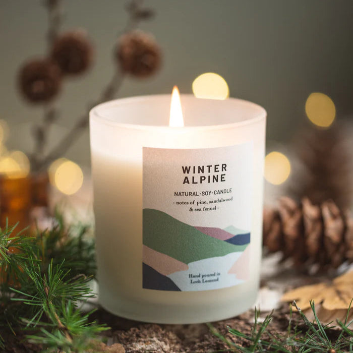 Frosted glass candle, lit, with "Winter Alpine" label.  Natural soy candle with pine, sandalwood, and sea fennel notes.