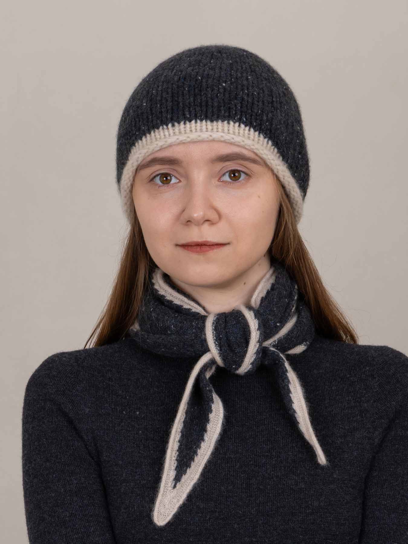 Person wearing a dark knitted hat and scarf against a plain background