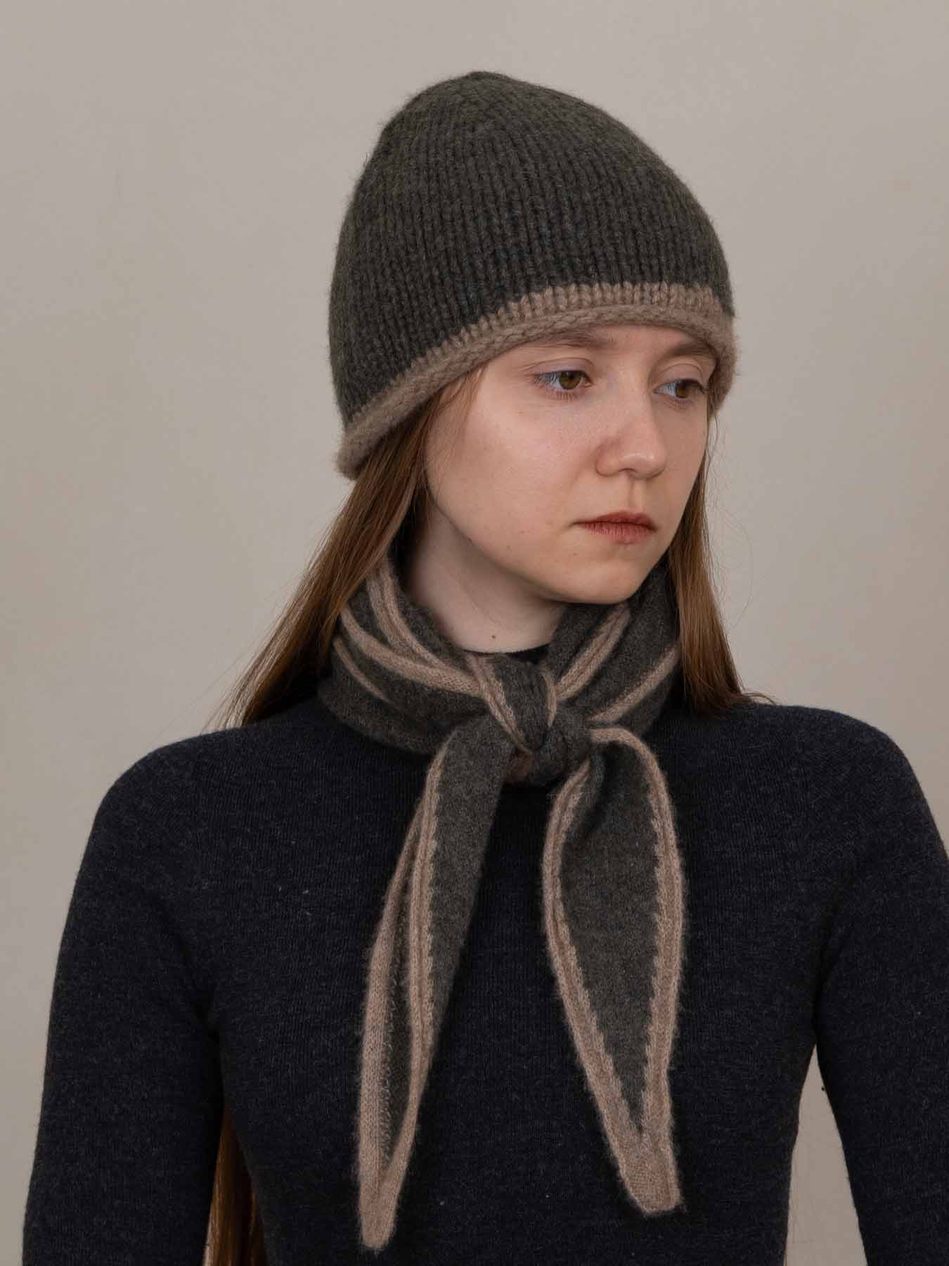 Woman wearing a dark knit hat and scarf against a plain background