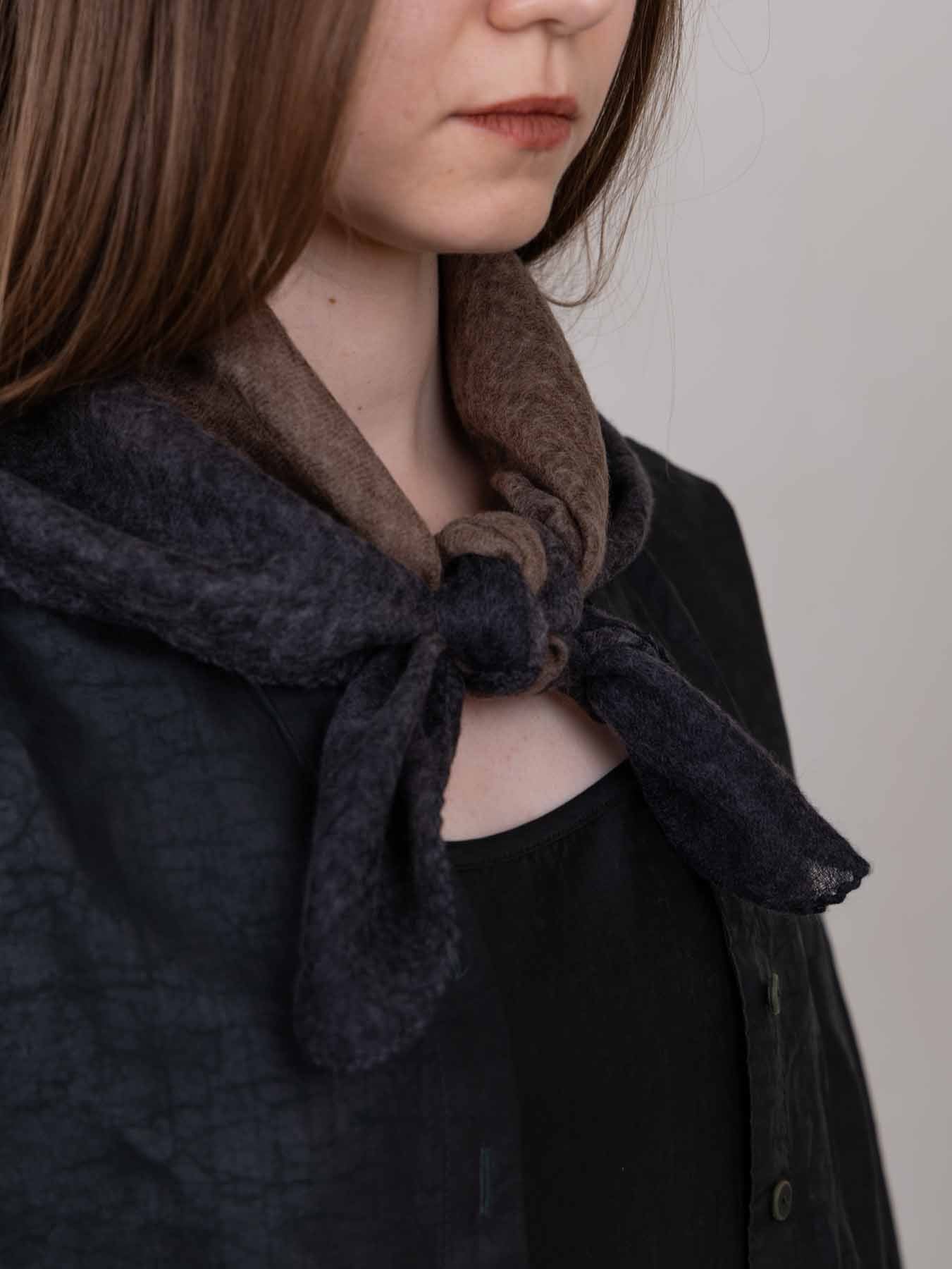 Person wearing a dark coat with a brown scarf tied around their neck against a plain background