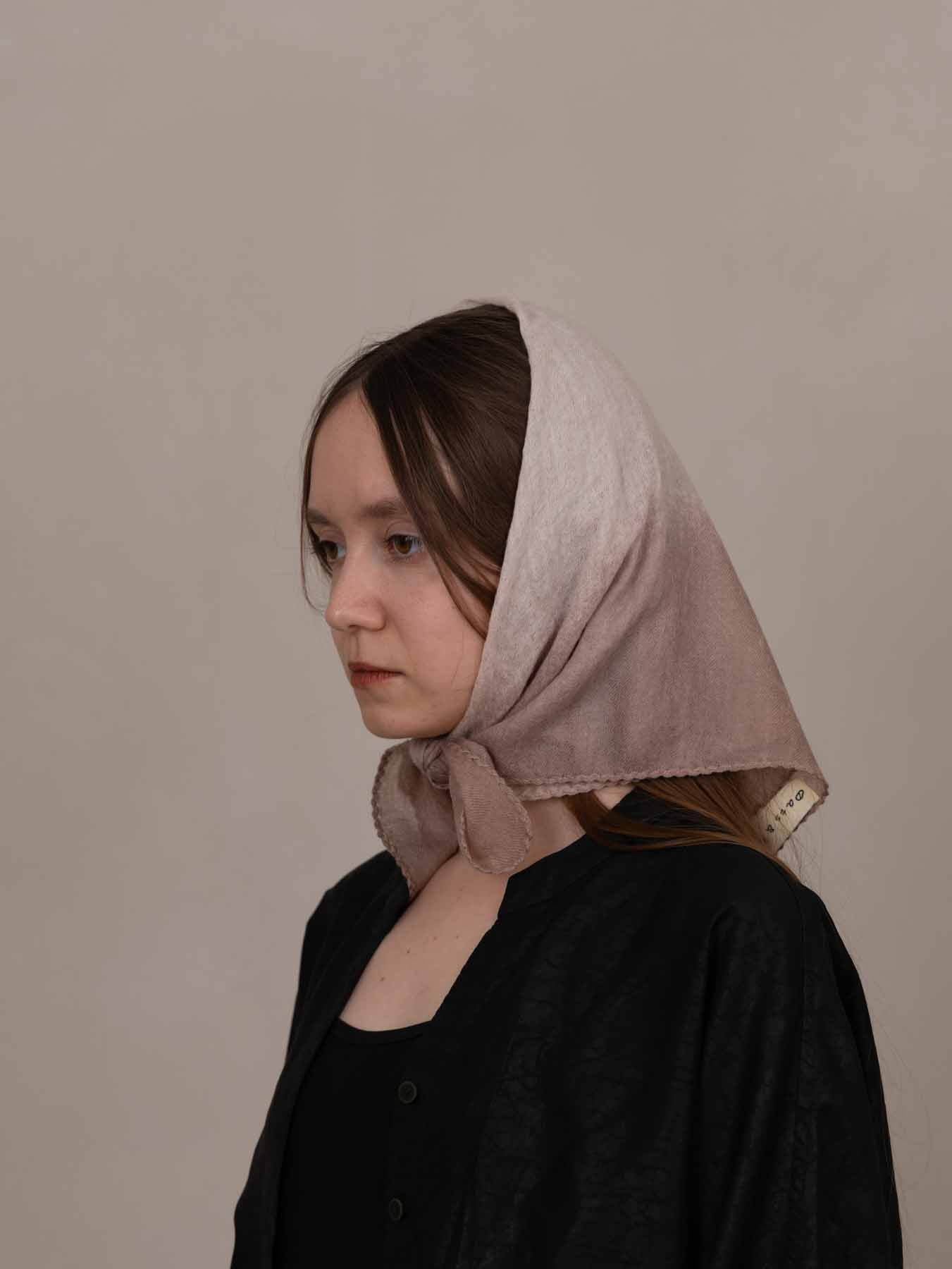 Woman wearing a beige headscarf against a plain background