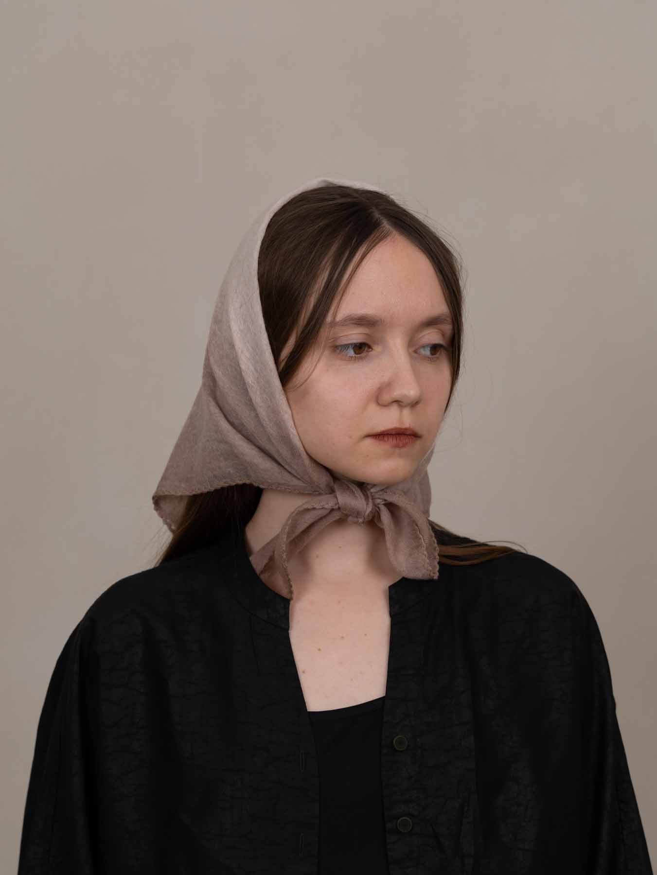Woman wearing a beige headscarf against a plain background