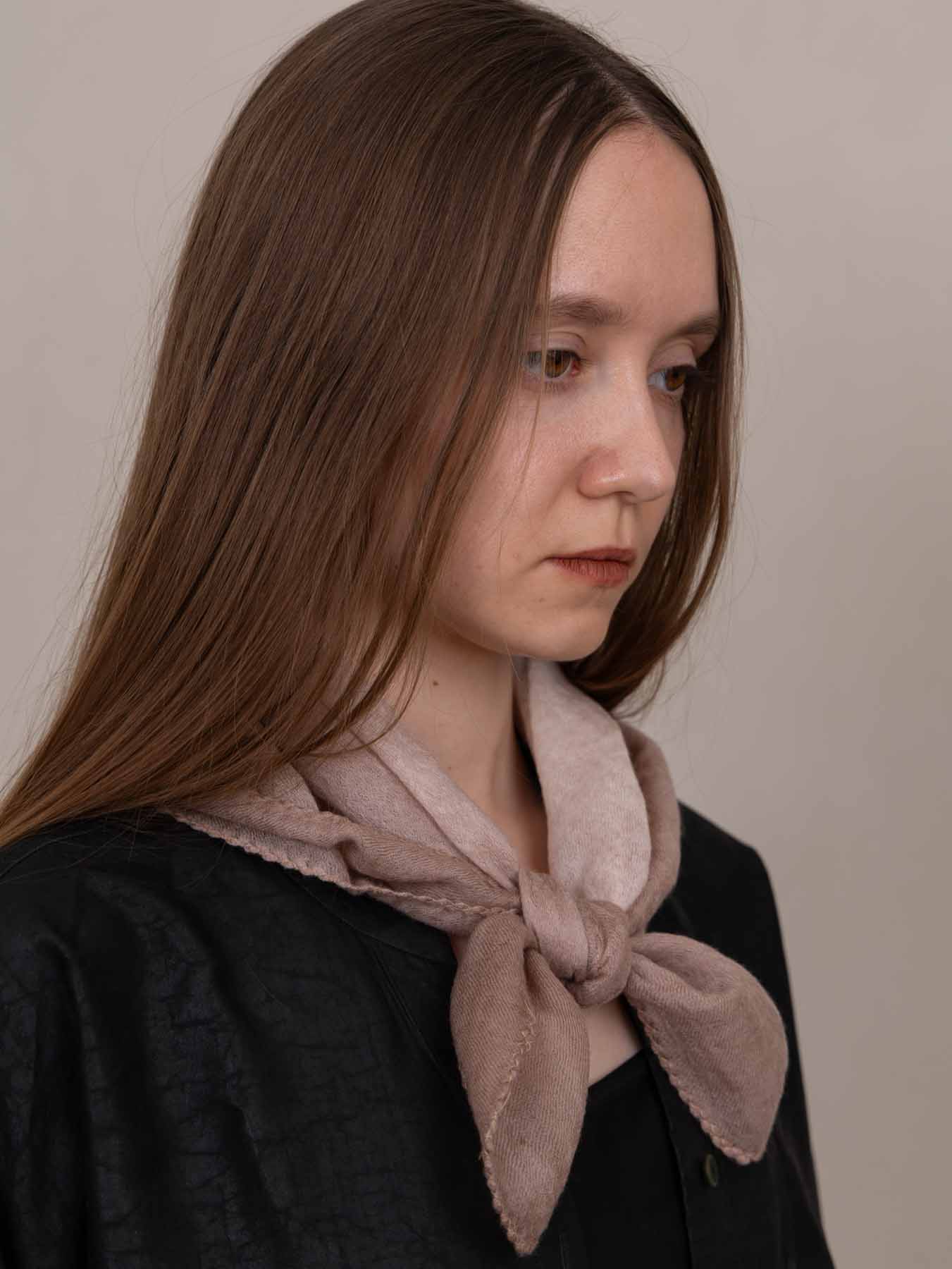 Woman wearing a light pink scarf against a plain background