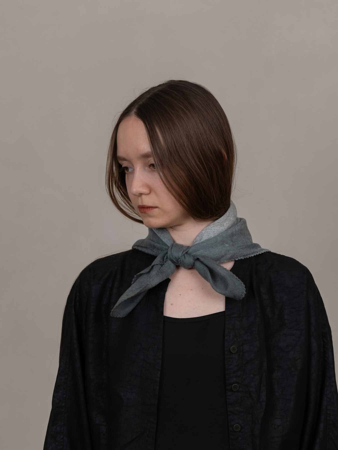 Woman wearing a dark jacket with a light blue scarf around her neck against a plain background