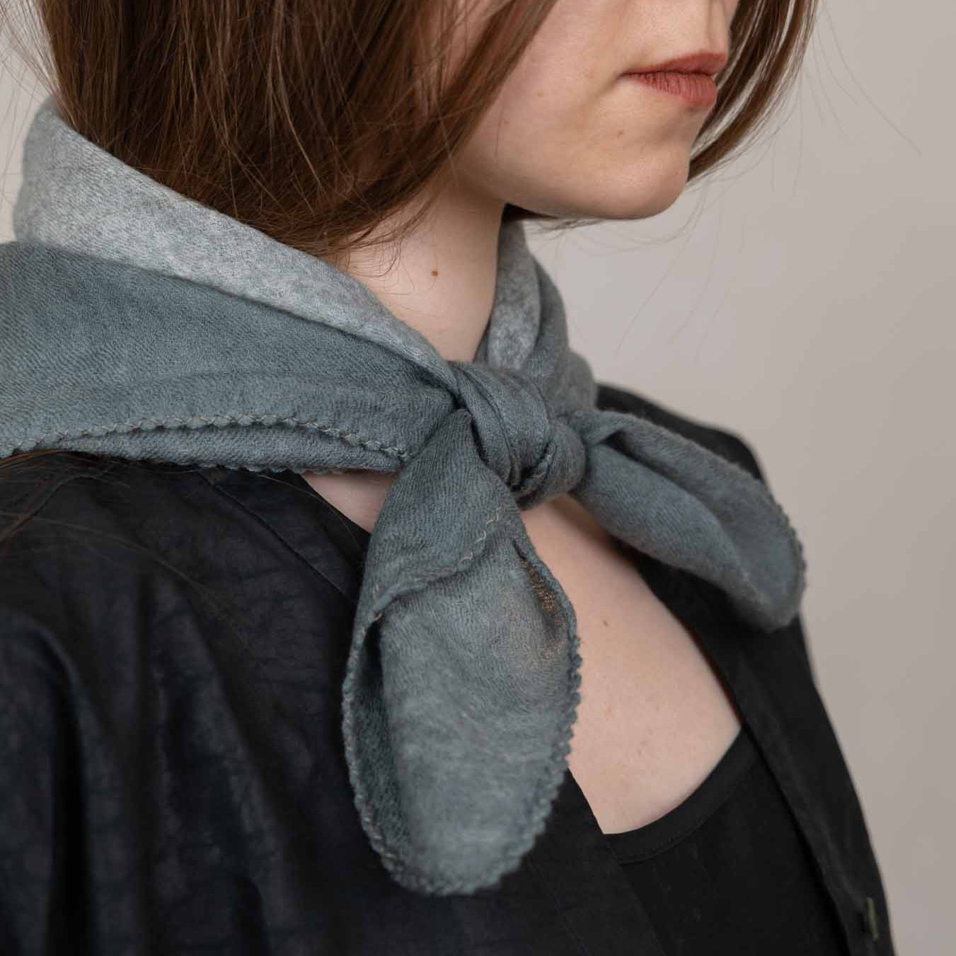 Person wearing a knotted gray scarf on a plain background