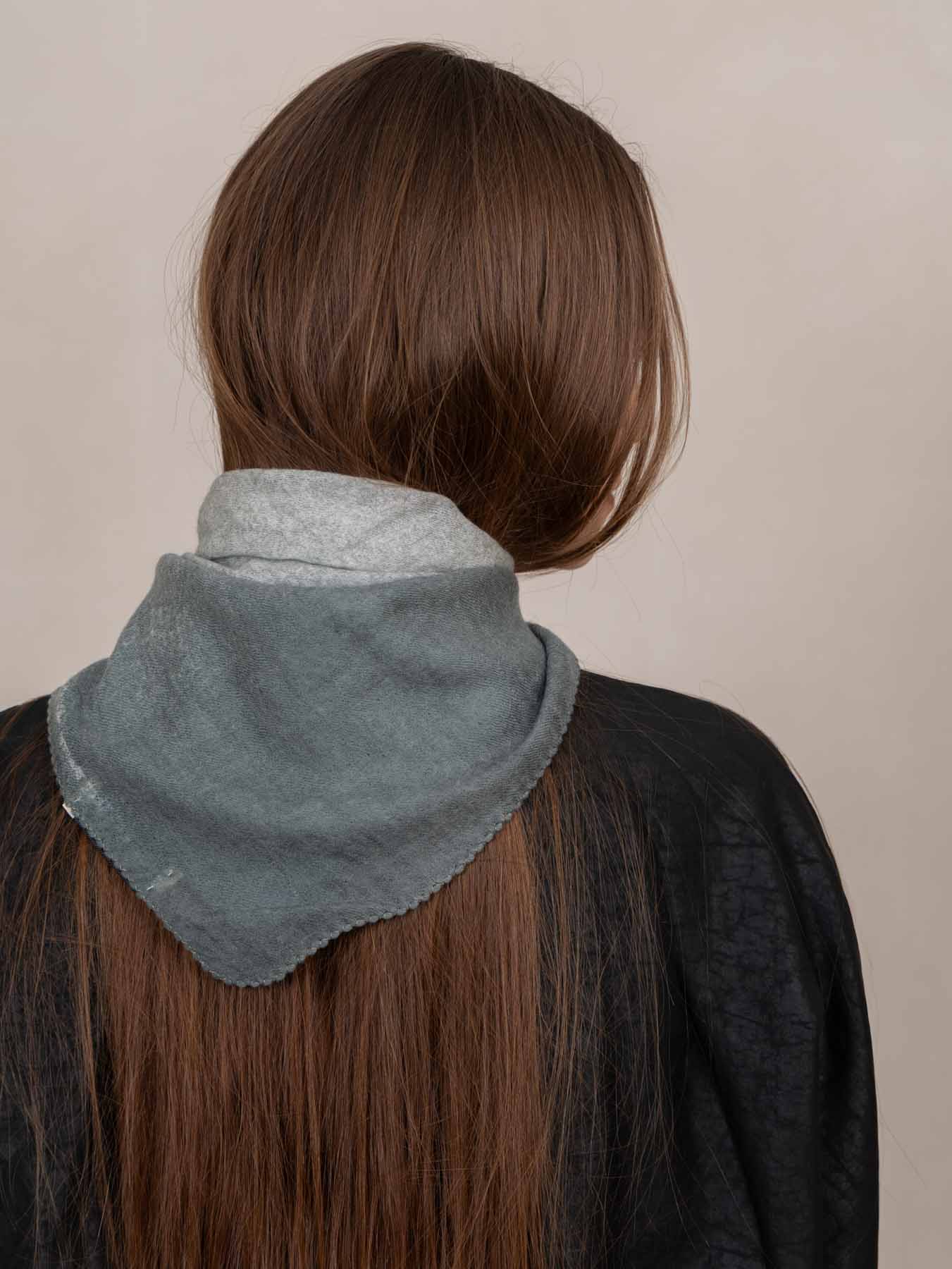 A person shown from the back wearing a light gray bandana-style hair wrap or scarf around their long brown hair, against a plain beige background.