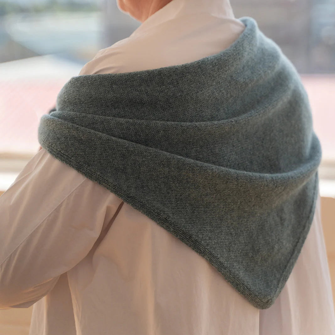 Person wearing a green shawl over a light-colored garment, standing indoors.