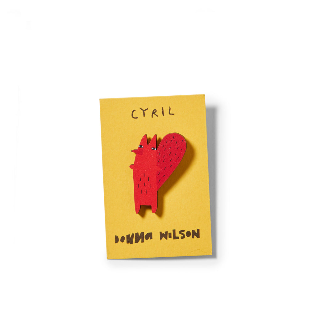 Red fox-shaped brooch on a yellow background, labeled "Cyril," by Donna Wilson.