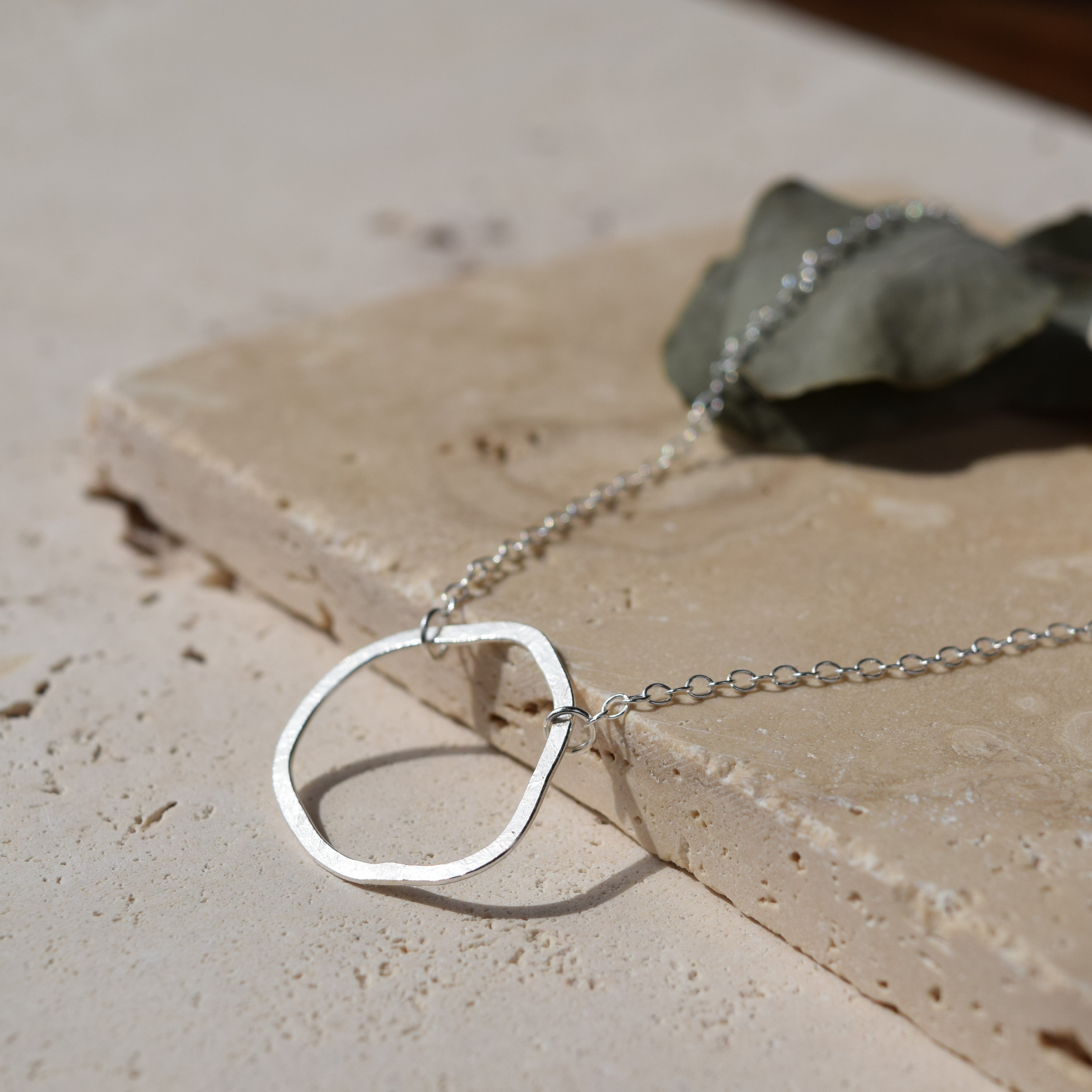 Silver hammered-metal pendant necklace with a simple, slightly irregular oval shape and a delicate chain.