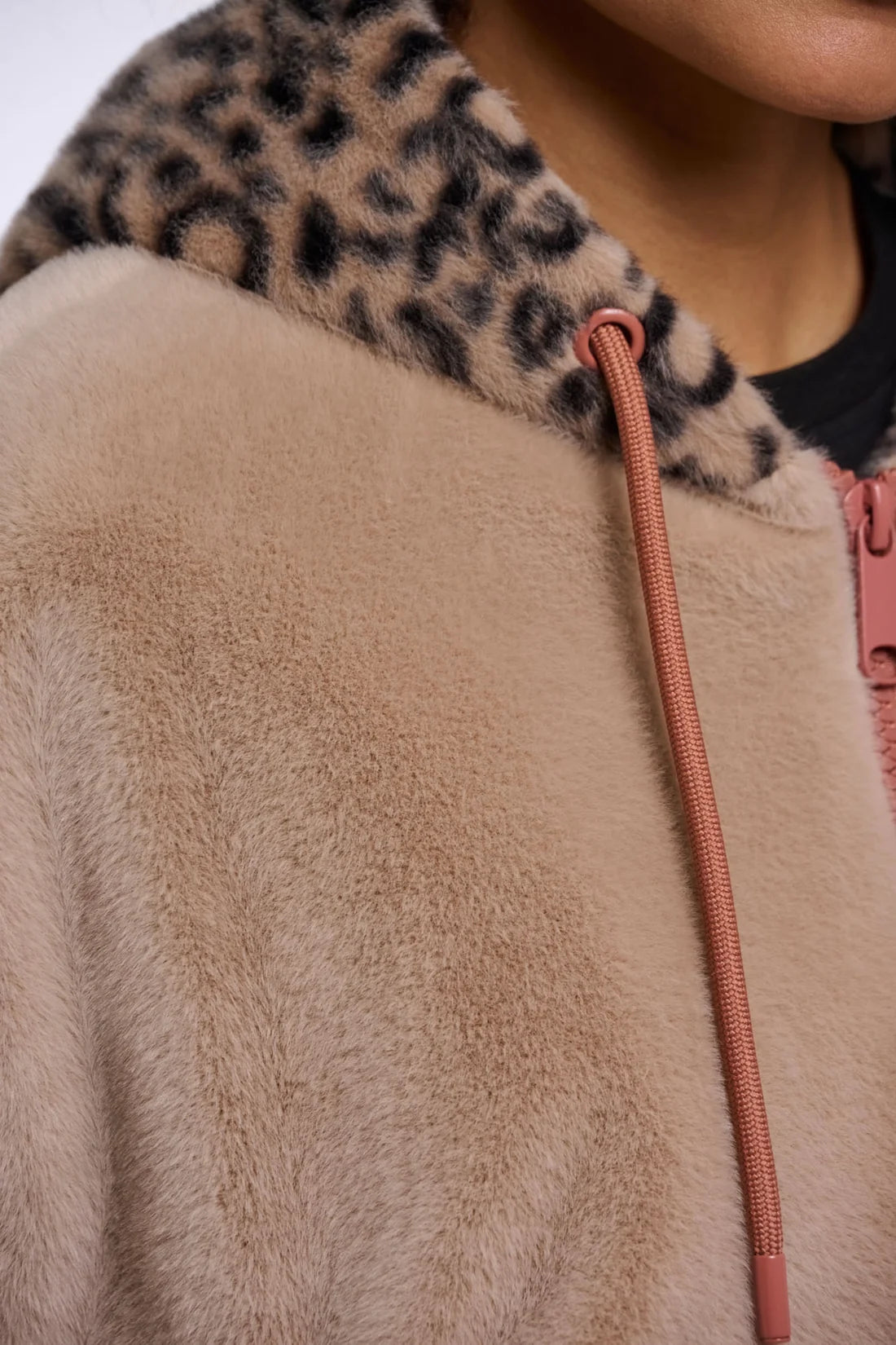 Close-up of a beige faux-fur zip jacket with a leopard-print hood and a pink drawstring.