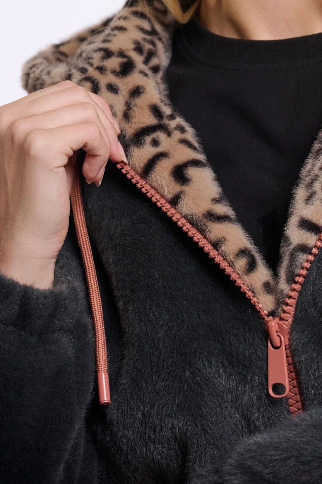 Close-up of a person wearing a dark fuzzy zip-up hoodie with a leopard-print collar and a rose-gold zipper and drawstring.