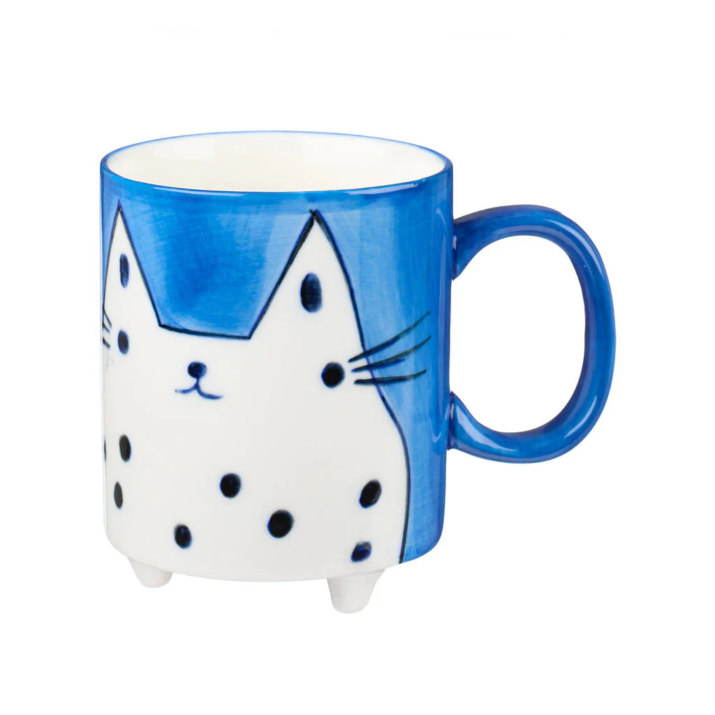 Blue mug with a hand-painted white cat design featuring black spots and whiskers.  The mug has small feet.