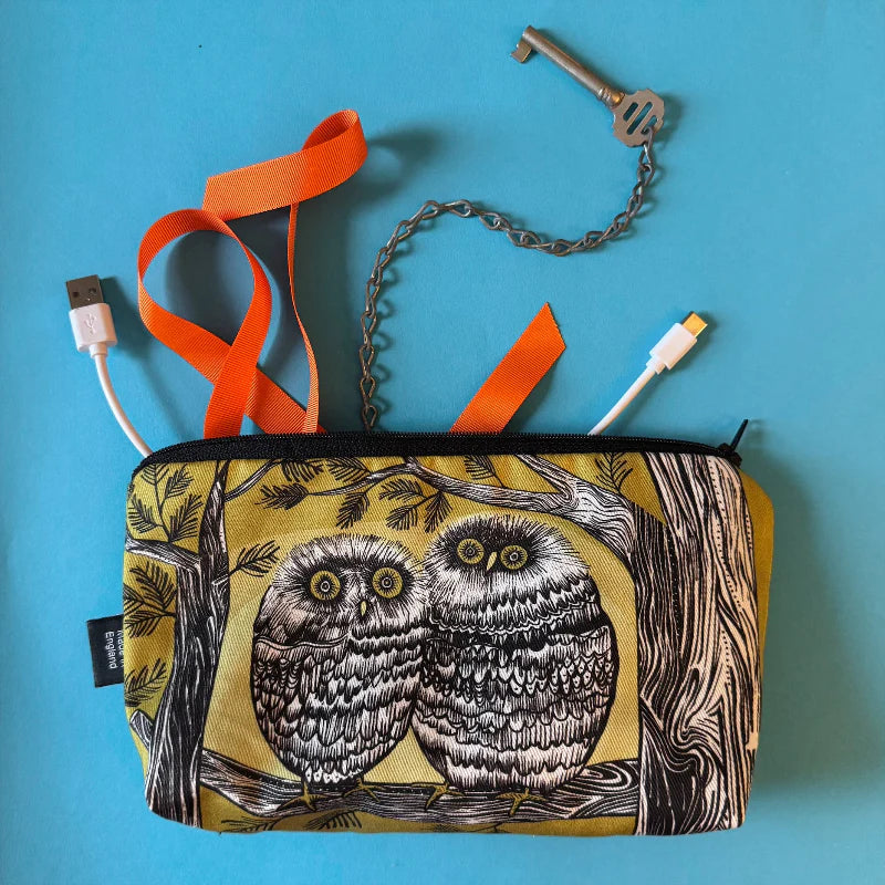 Pouch with owl design, USB cable, key, and orange strap on a blue background