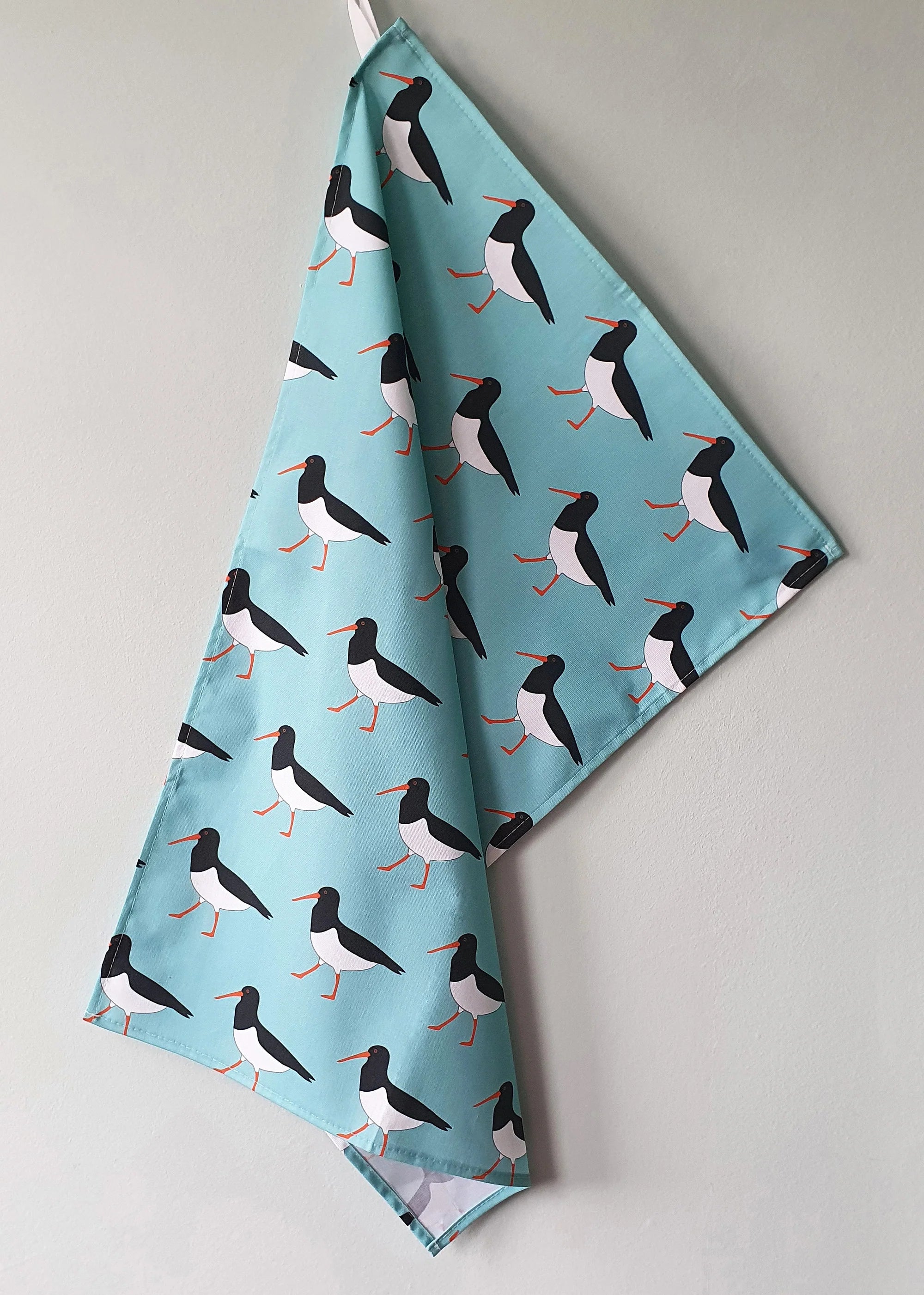 Fabric with bird pattern on a light blue background, hanging against a gray wall.
