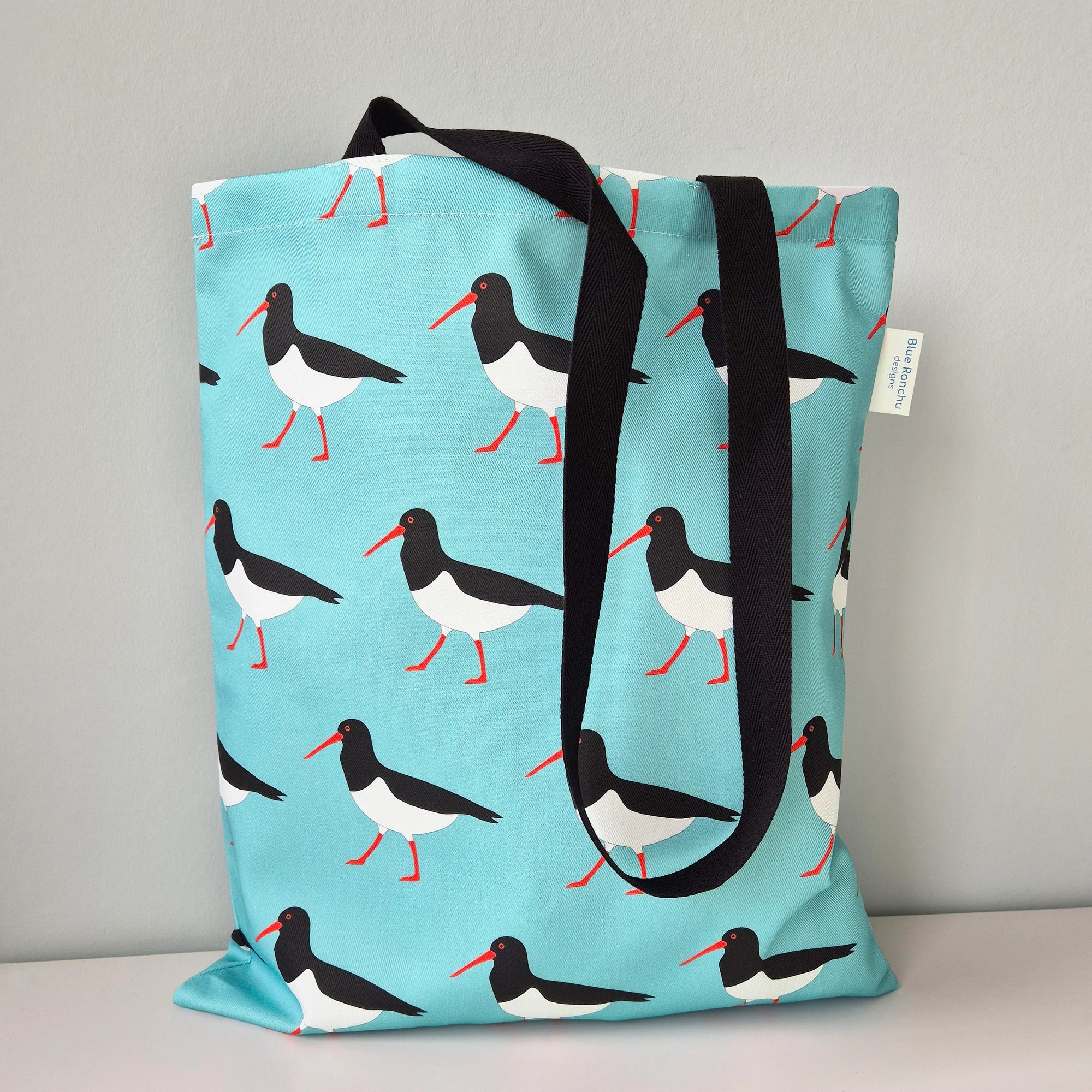 Tote bag with bird pattern and black handles on a gray background