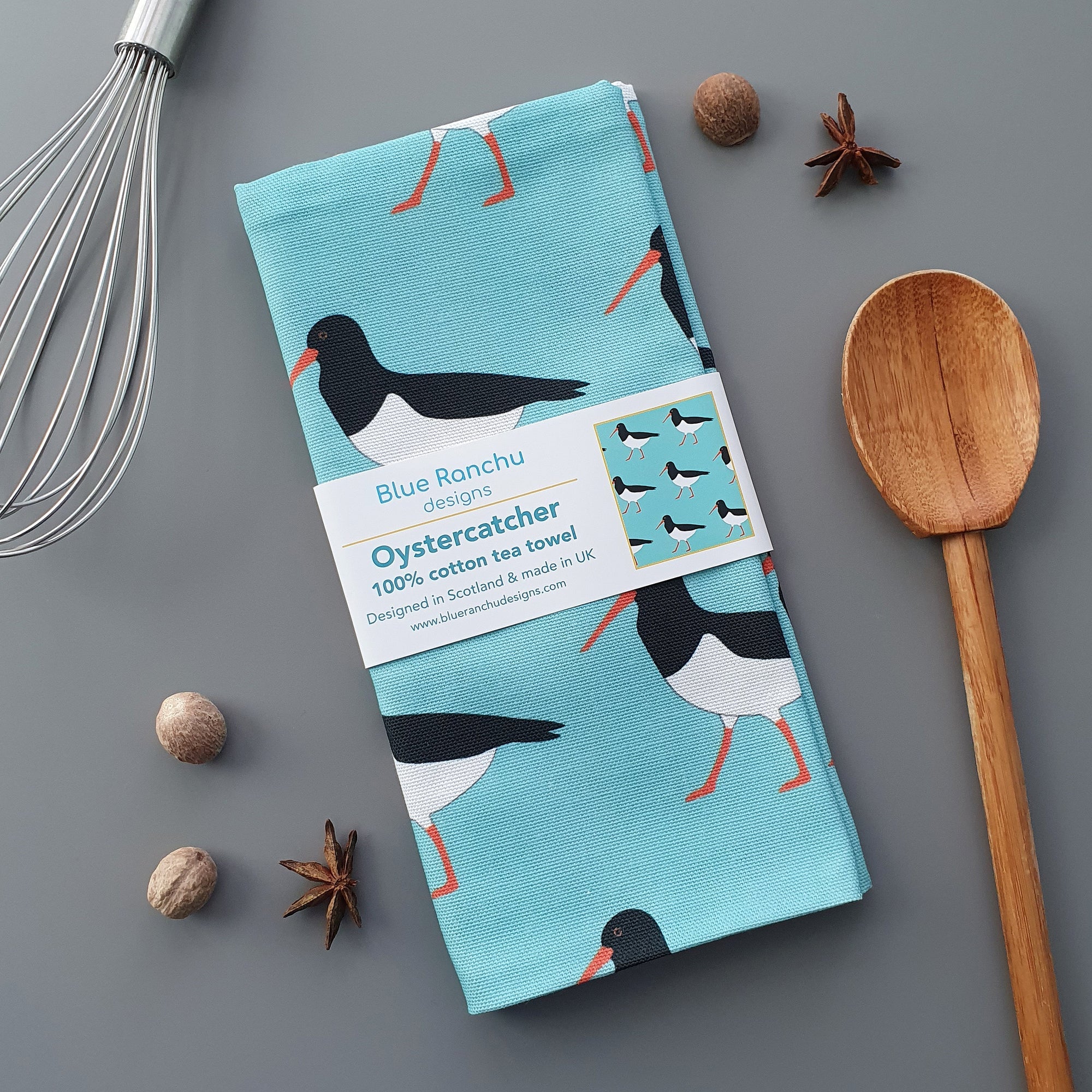 Tea towel with oystercatcher design by Blue Ranchu on a gray background with kitchen items.