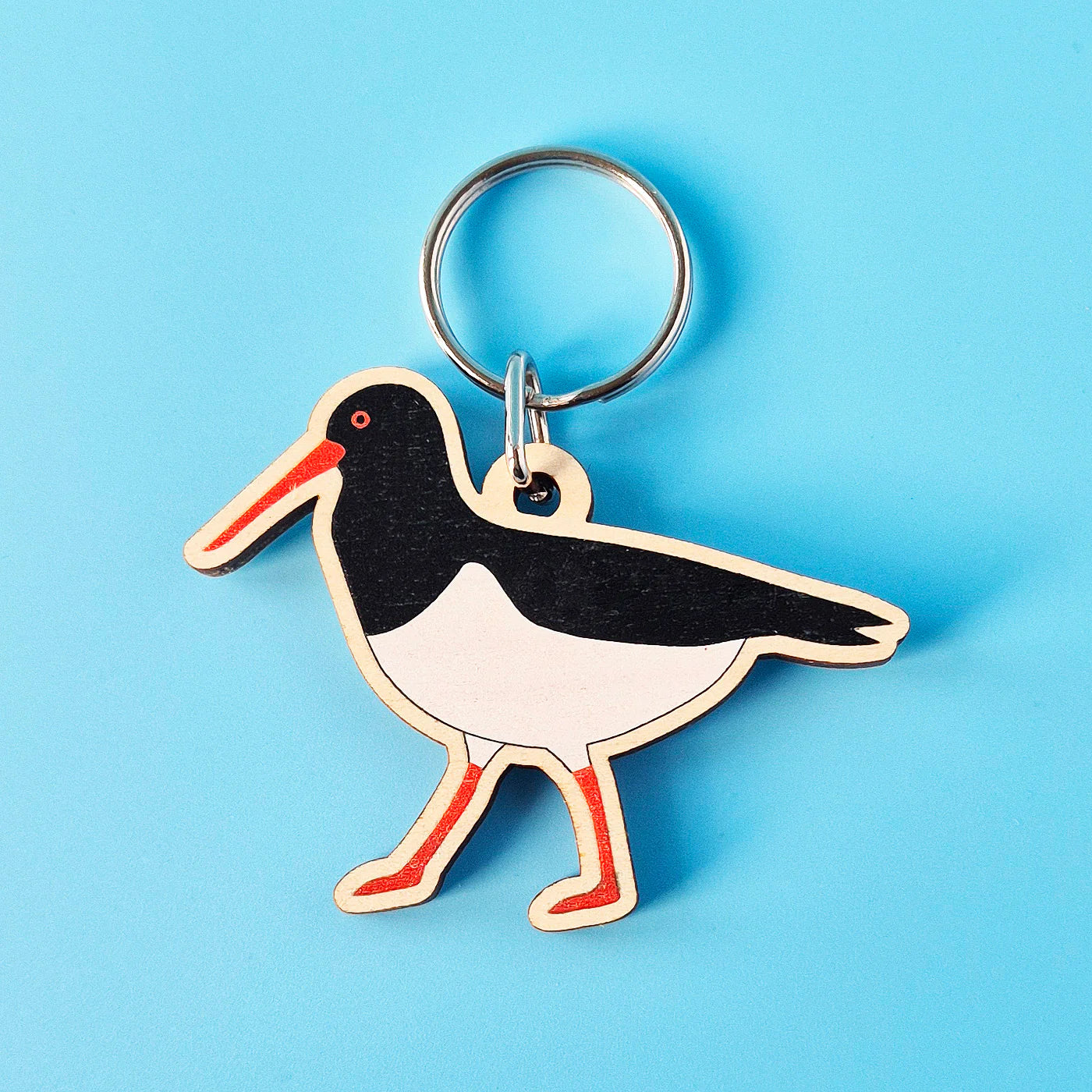 Wooden keychain shaped like a bird with a red beak on a blue background