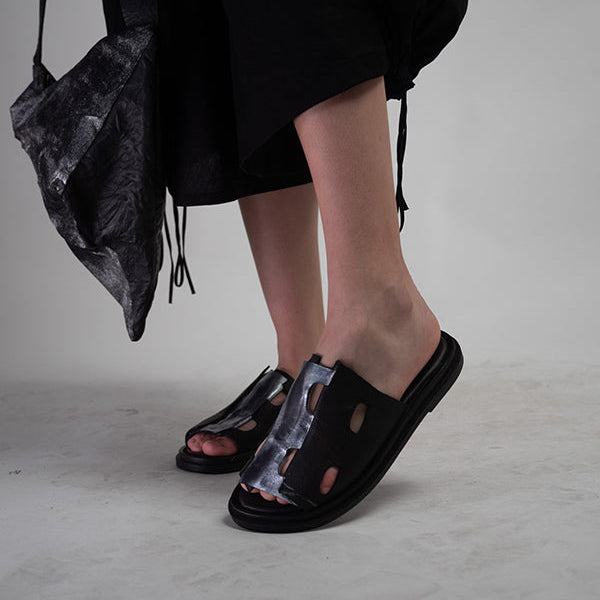 Black leather slide sandals with cutout detailing and a metallic silver accent.