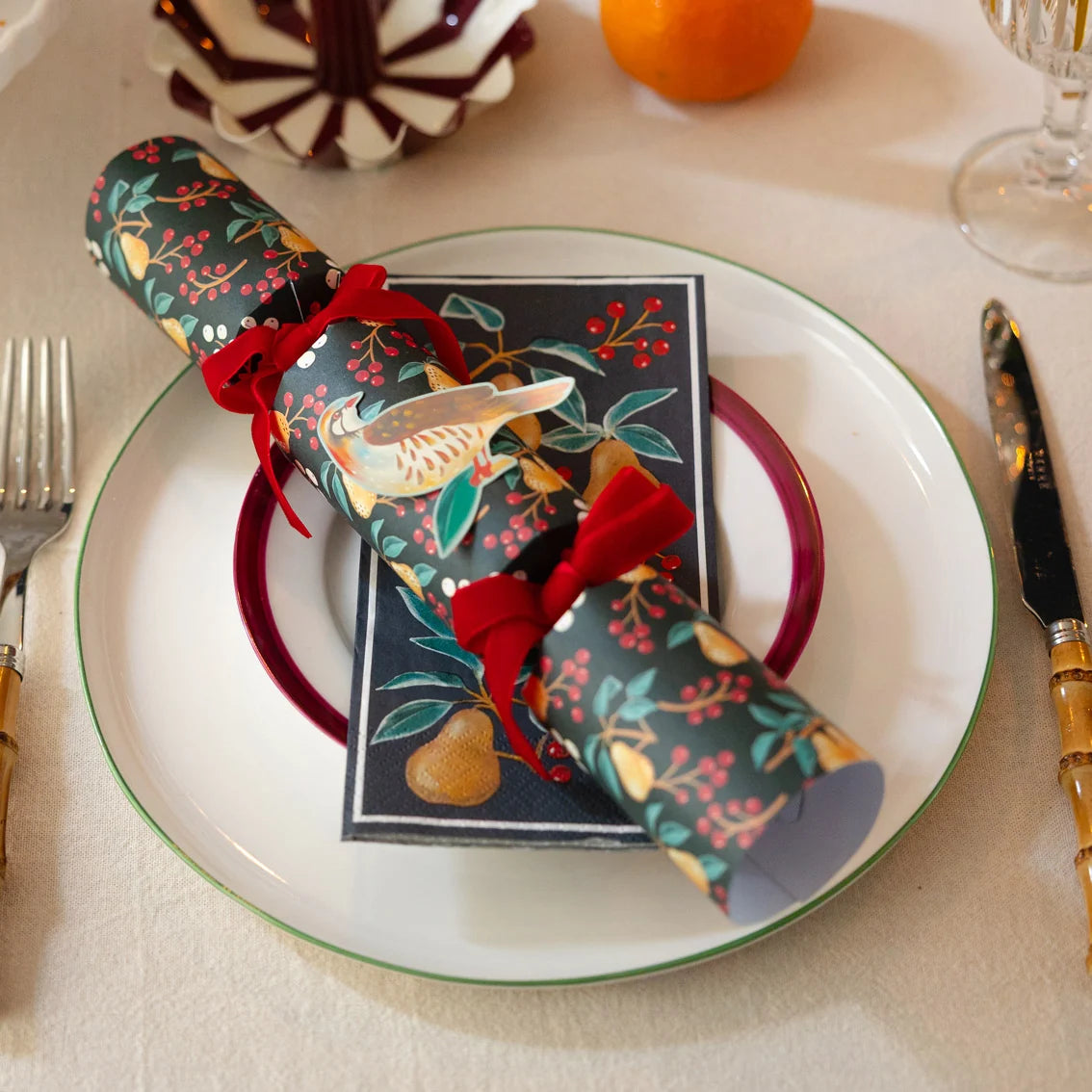 Decorative Christmas cracker with a card on a plate with cutlery and a glass.