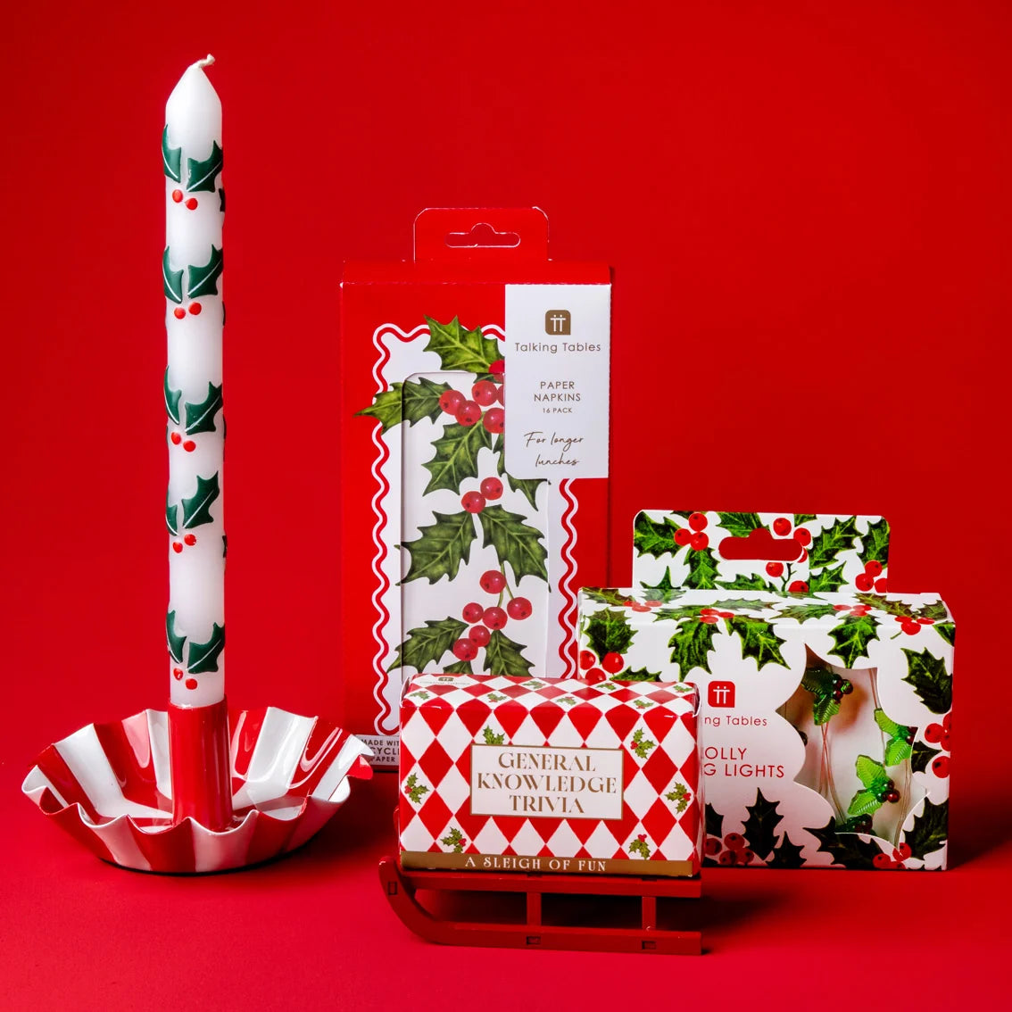 Christmas-themed products including a candle, napkins, and a trivia game on a red background