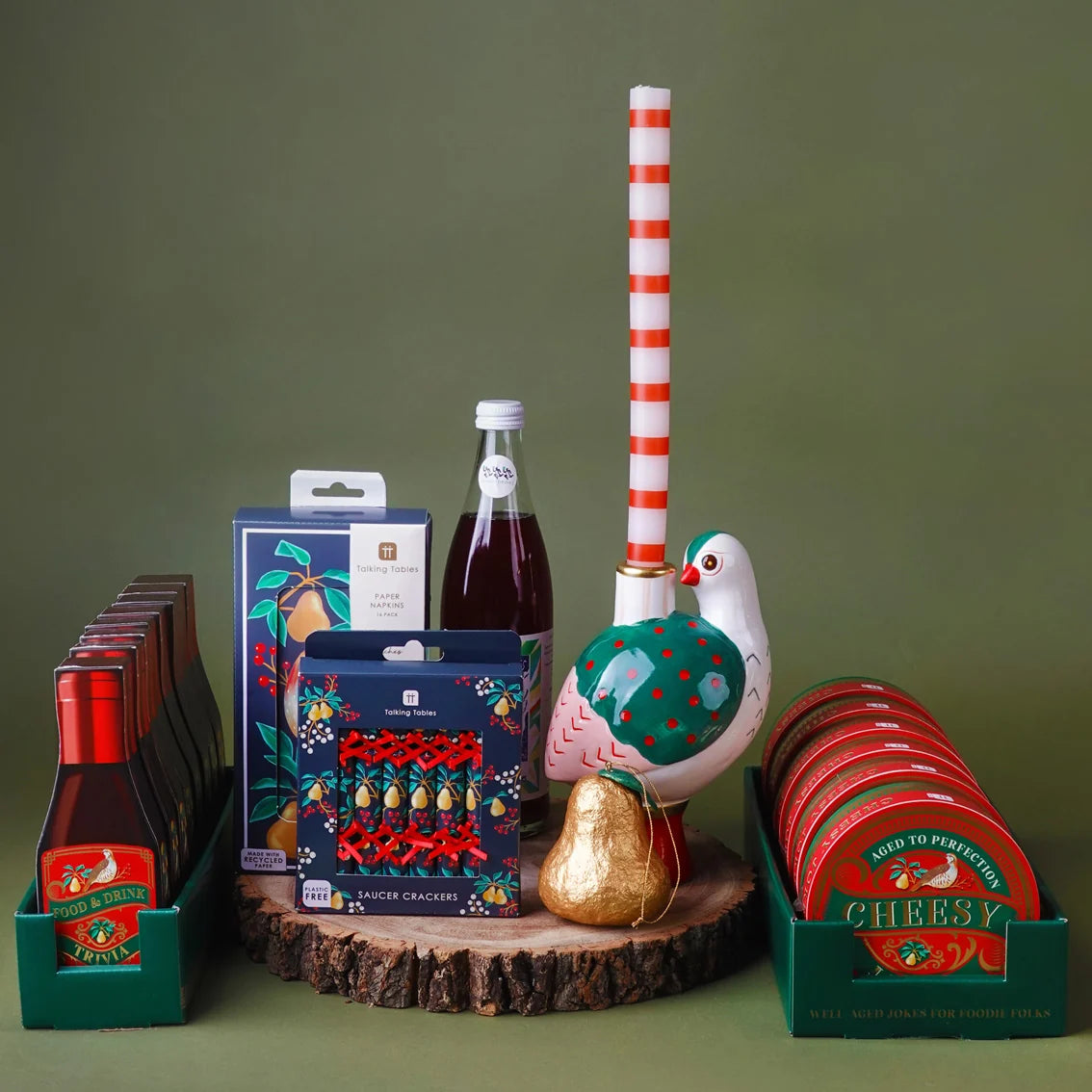 Collection of Christmas-themed products including bottles, boxes, and a decorative bird on a green background