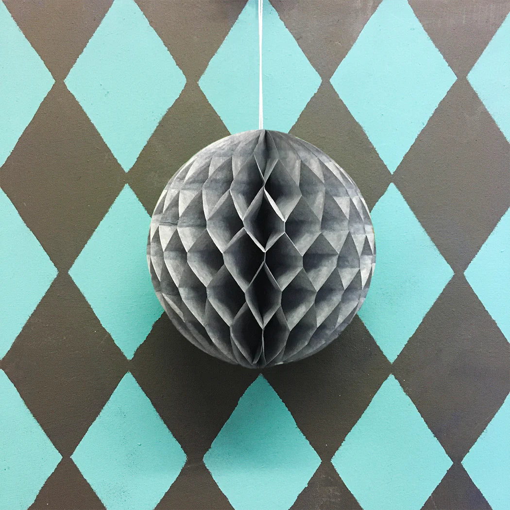Gray honeycomb paper ball hanging against a teal and brown diamond patterned background.