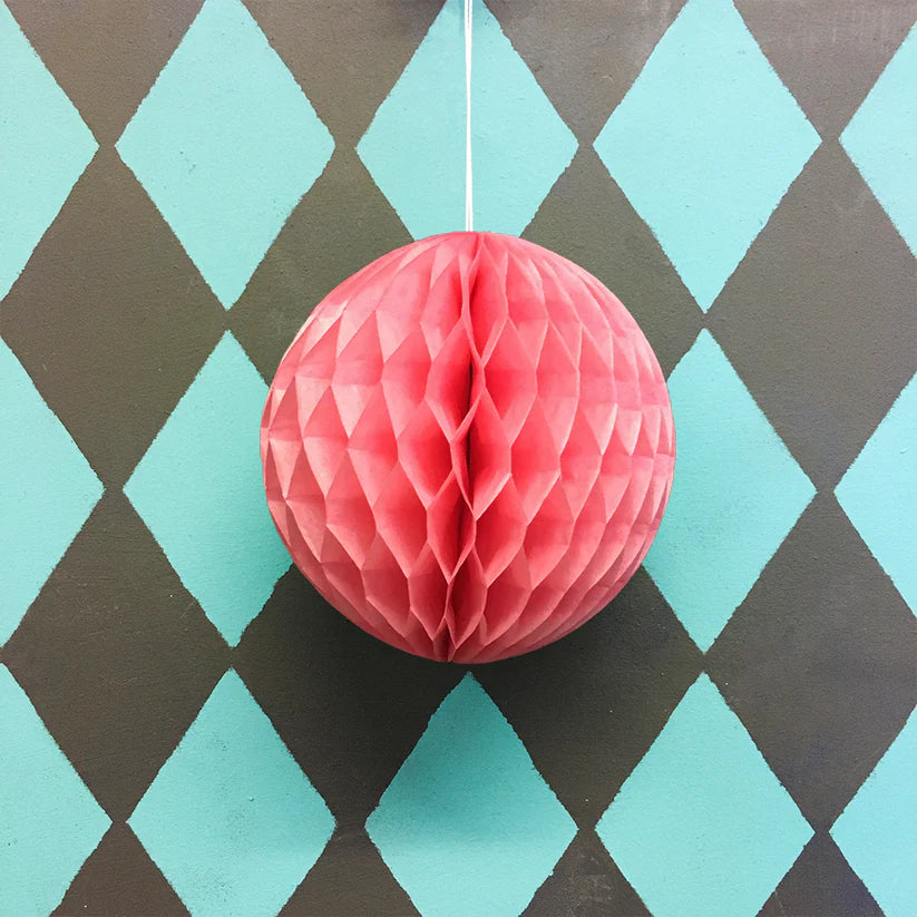 Pink honeycomb paper ball hanging against a teal and brown diamond patterned background.