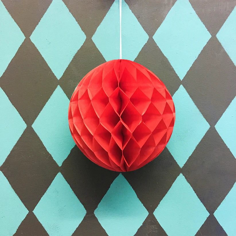 Red honeycomb paper ball hanging against a teal and brown diamond patterned background.
