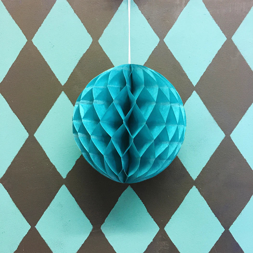 Teal honeycomb paper ball hanging against a brown and teal diamond patterned background.