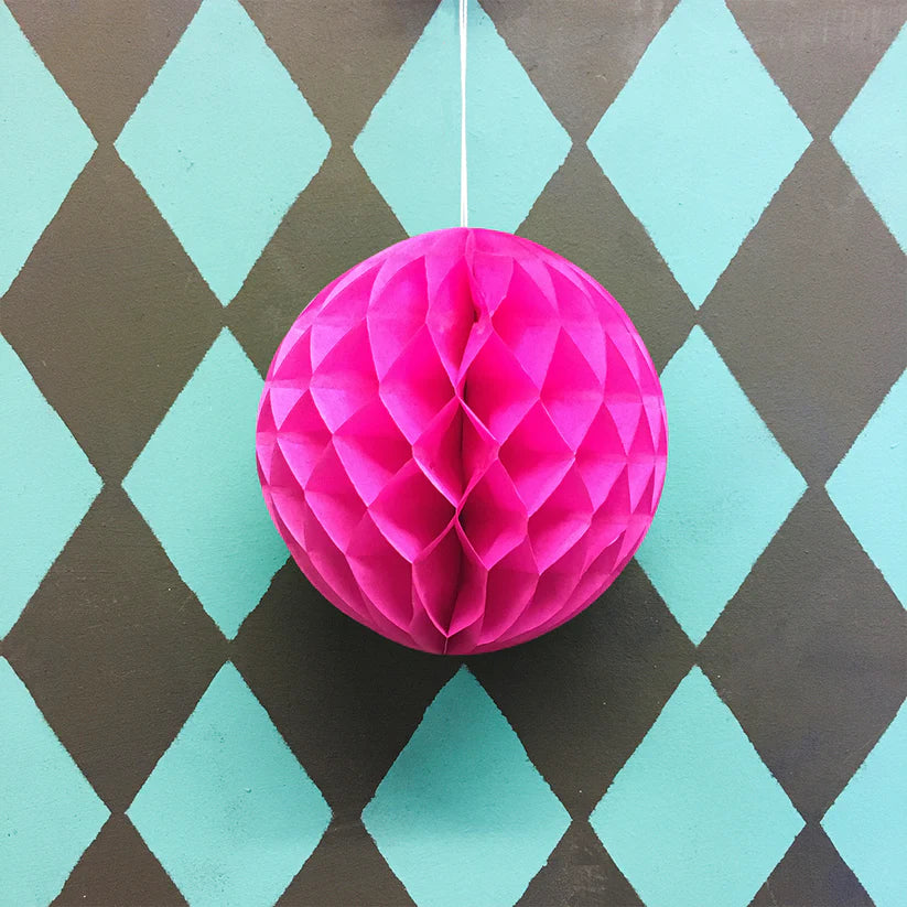 Pink honeycomb paper ball hanging against a teal and brown diamond patterned background.