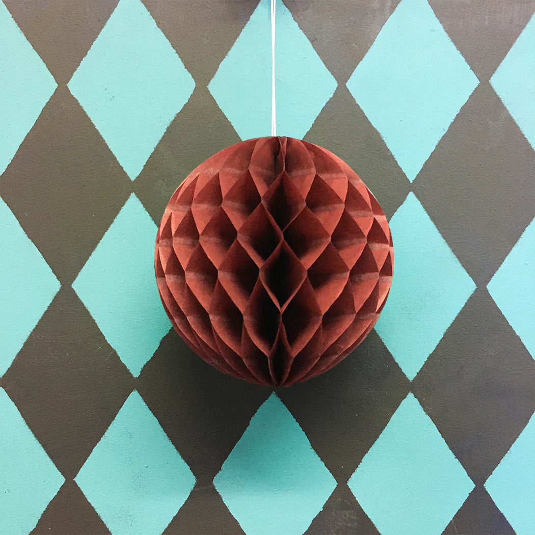 Dark red honeycomb paper ball hanging against a teal and brown diamond pattern background.