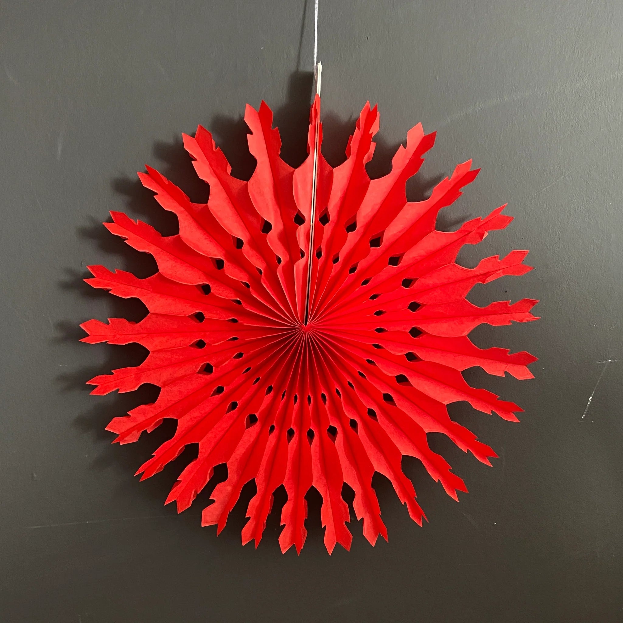 Red paper snowflake decoration with a lacy, pleated design.